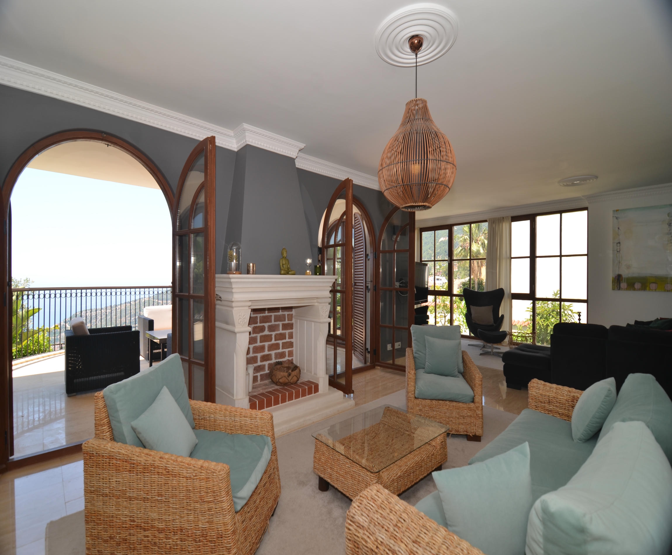 Living room with a brick fireplace and wicker furniture beside arched balcony doors in a villa