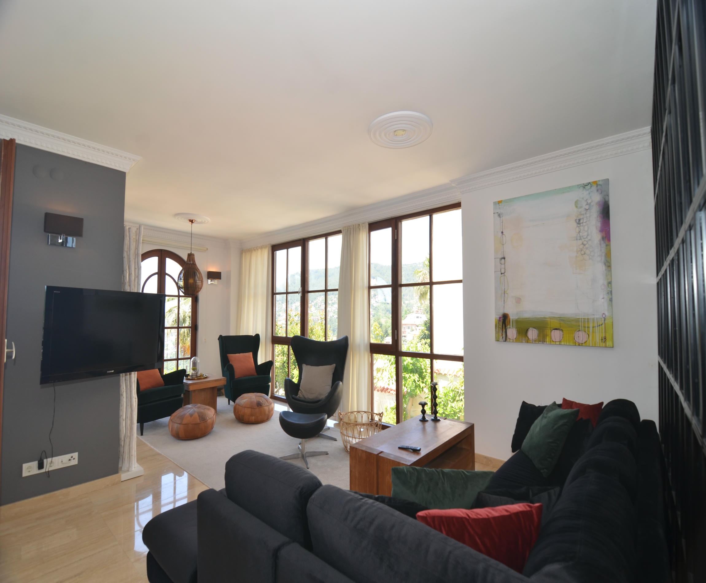 Living room with a dark corner sofa and two black chairs by panoramic windows in a villa for sale