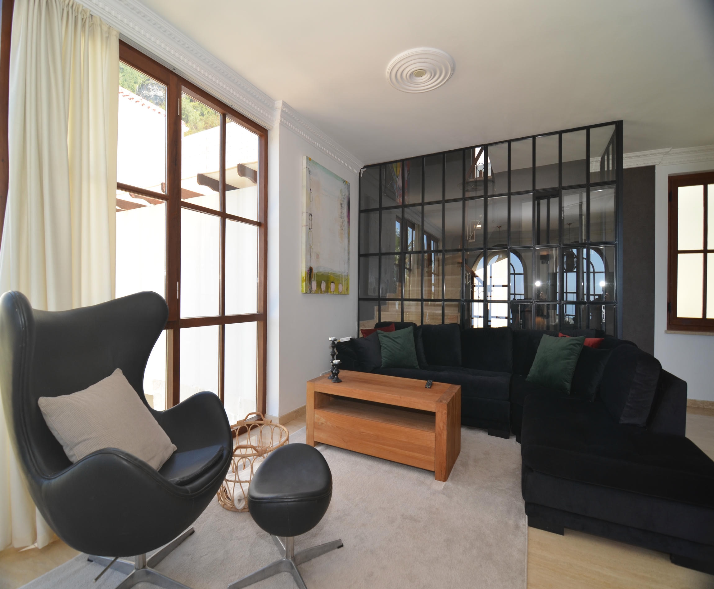 Living room with a dark sofa, black glazed partition and light rug in a home for sale in Turkey