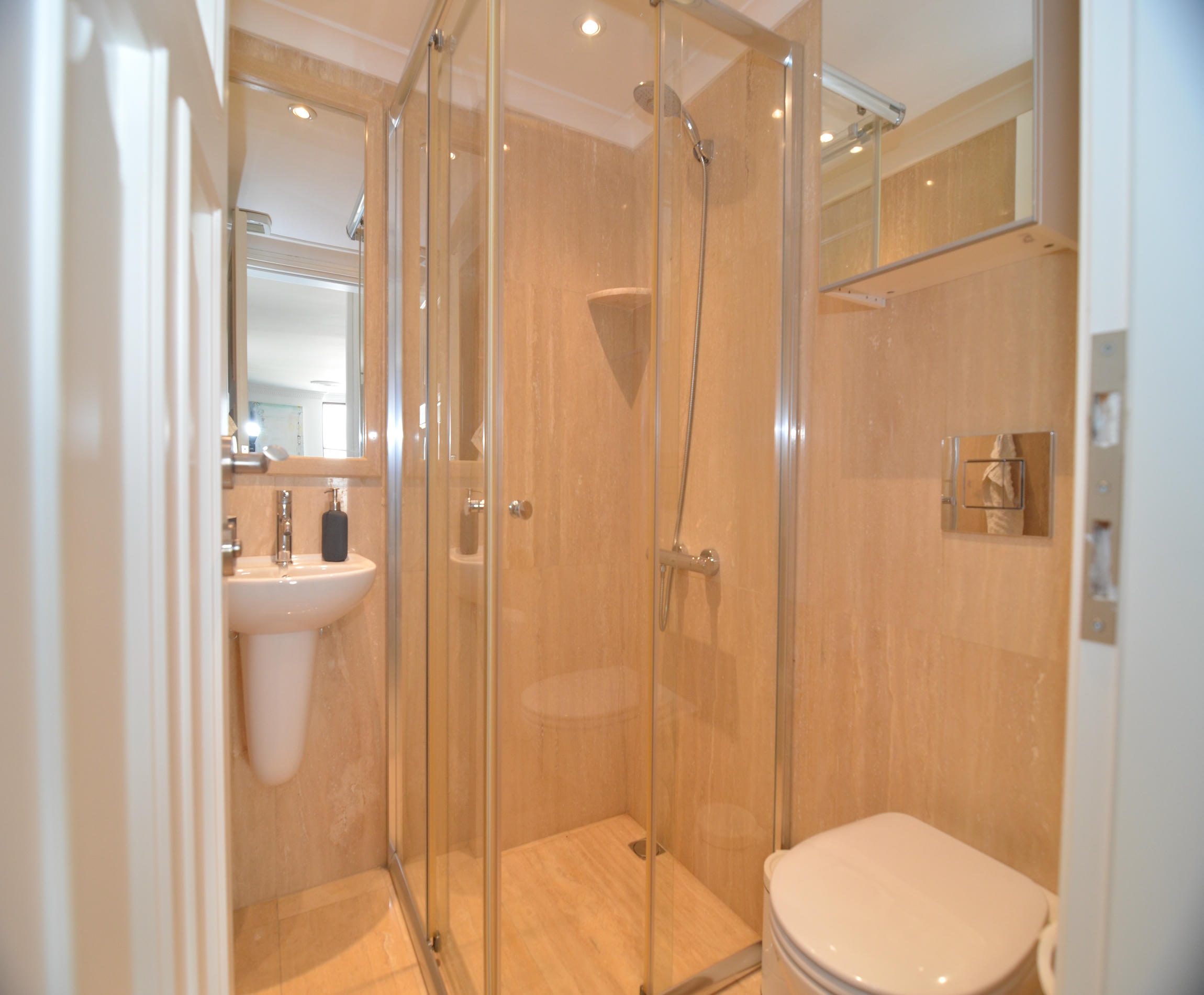 Bathroom with a glass shower cabin, wall-mounted basin and beige tile