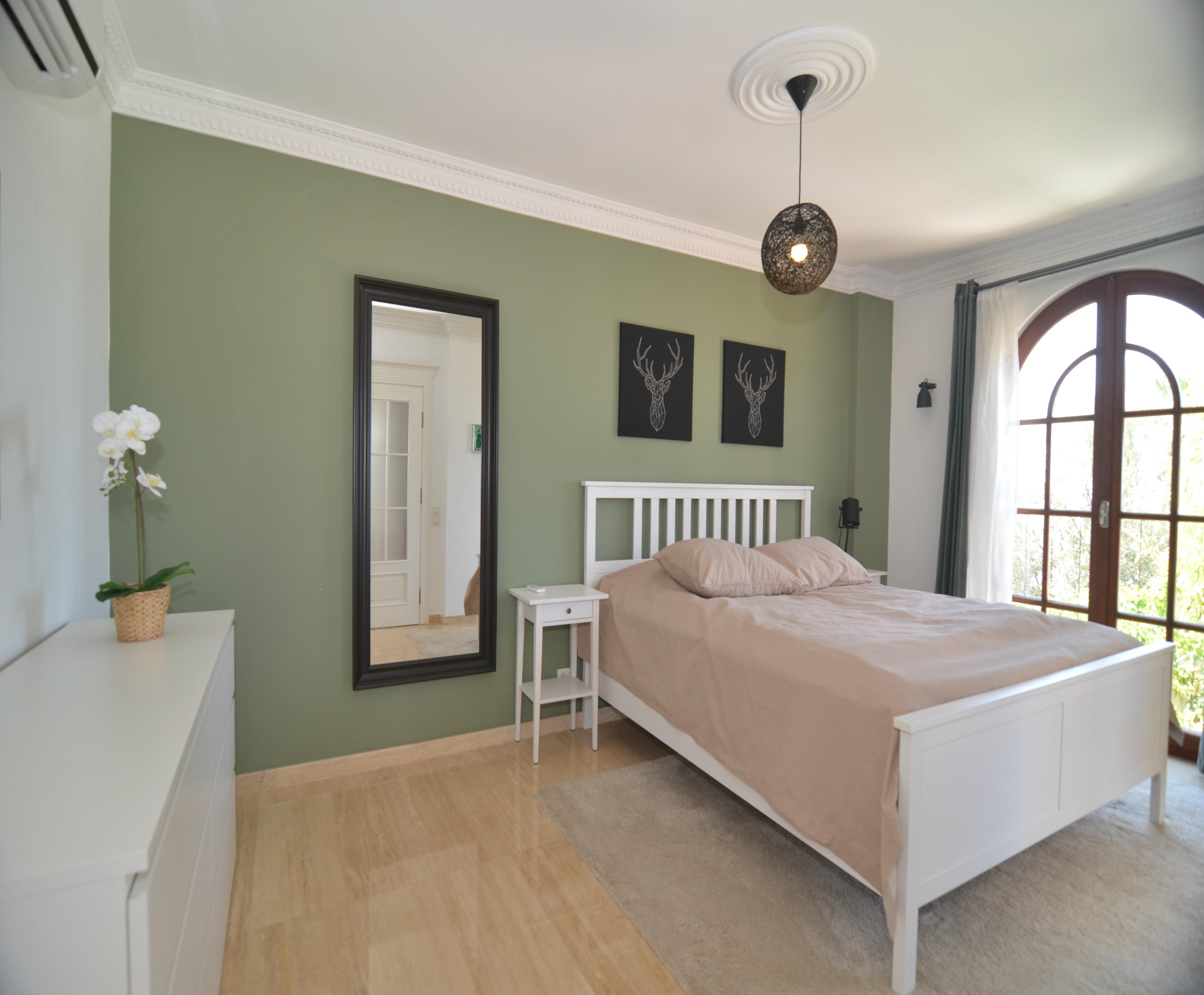 Bedroom with a white headboard, green accent wall and arched window in an Alanya house