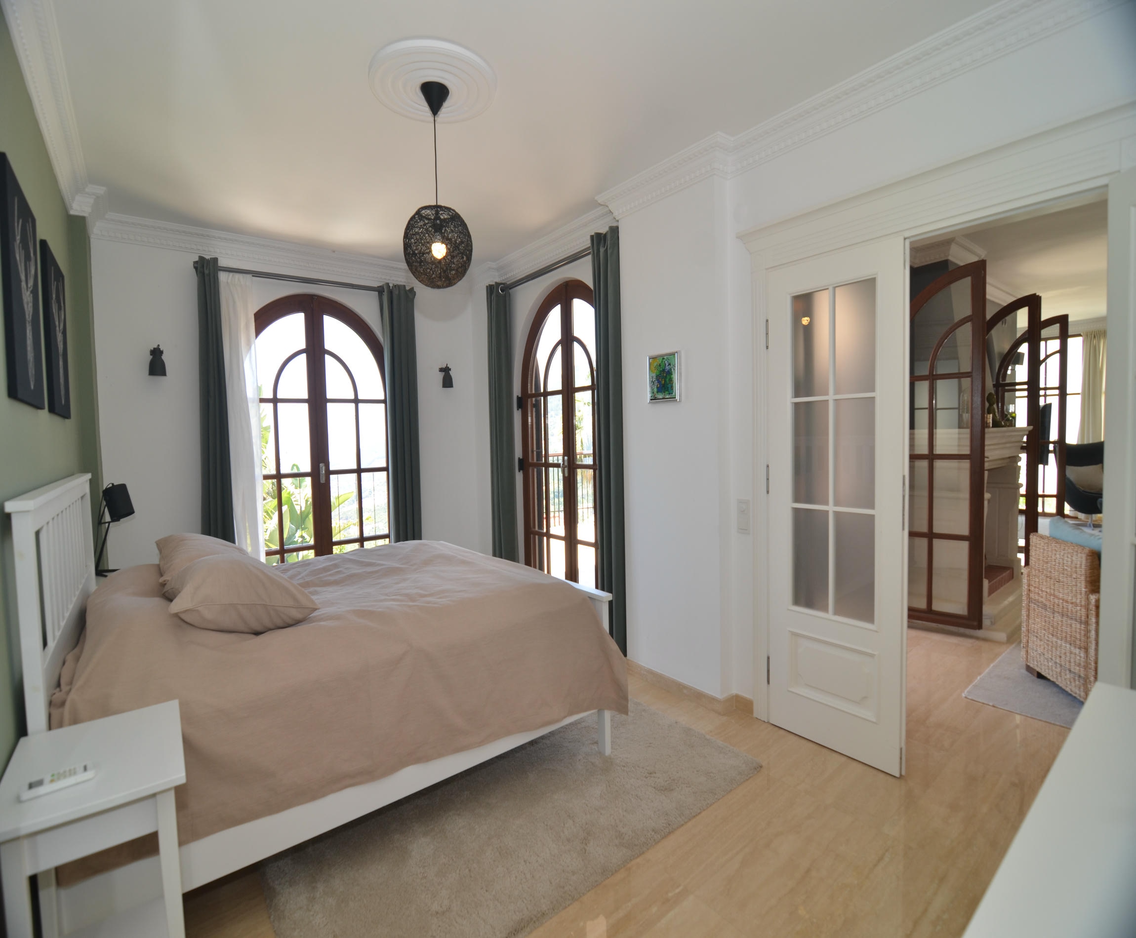Bedroom with a beige bed and arched wooden windows in a villa