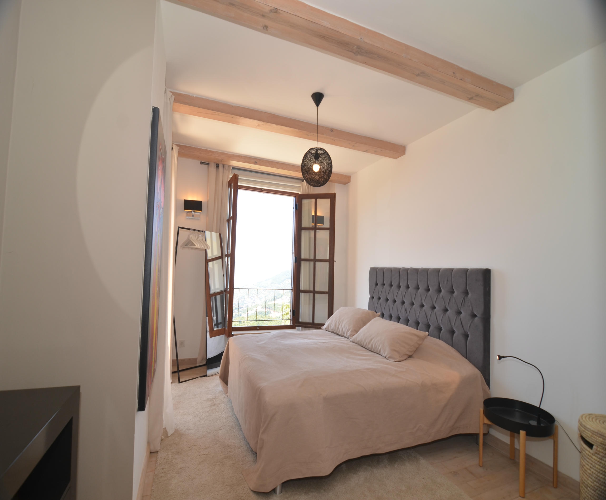 Bedroom with a gray quilted headboard, timber beams and wall-mounted television in Alanya