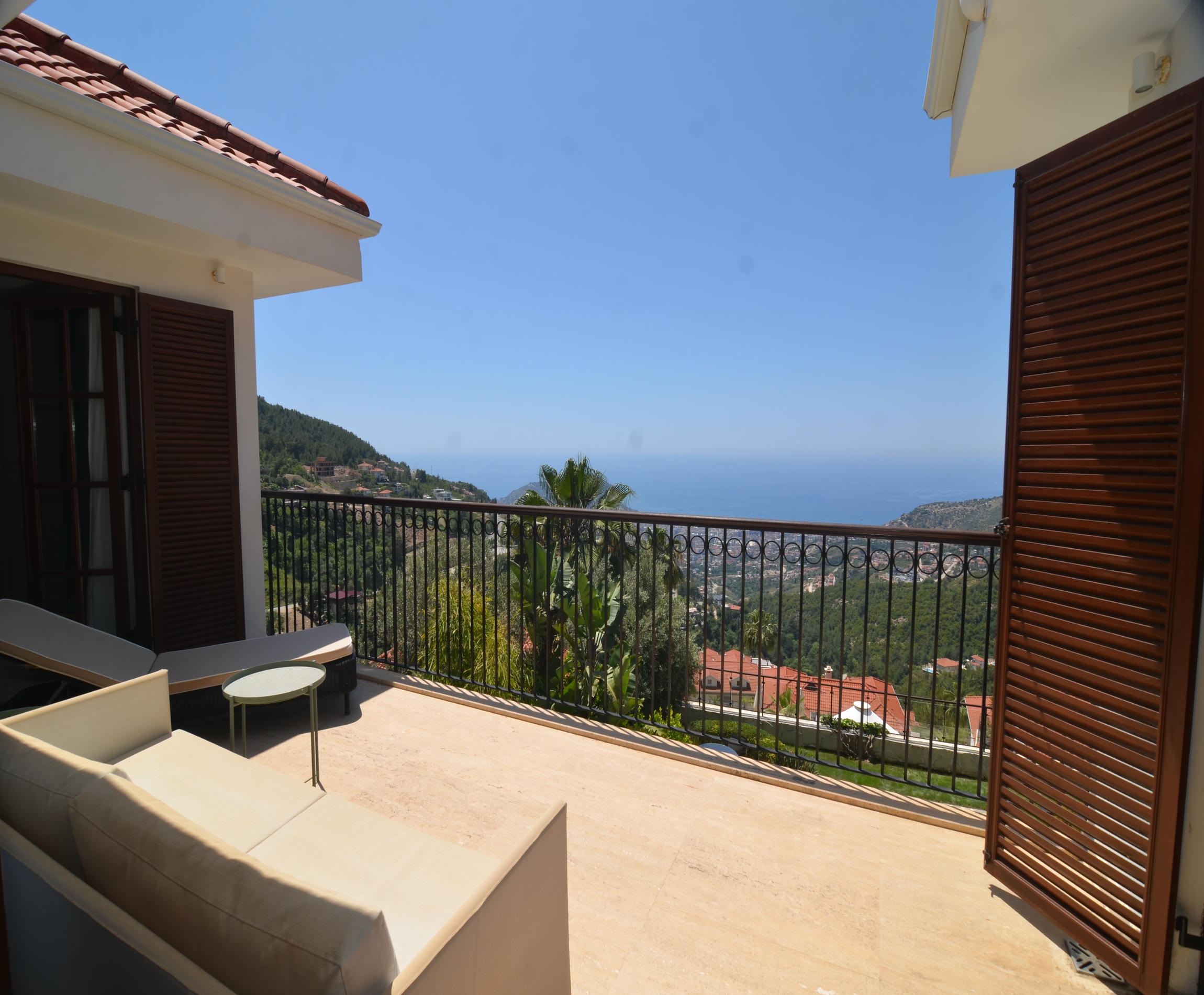 Spacious terrace of a villa with black metal railing, white chair and distant sea view