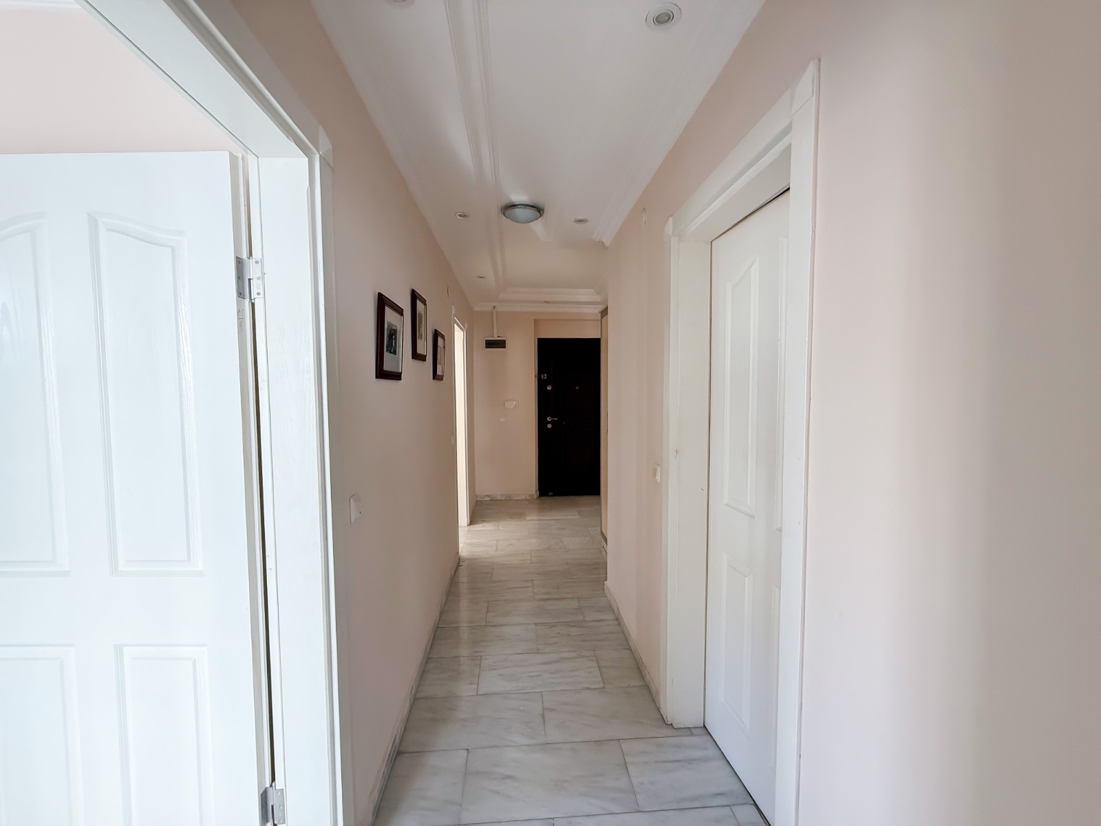 Bright hallway with marble flooring, white doors and framed wall art in a flat