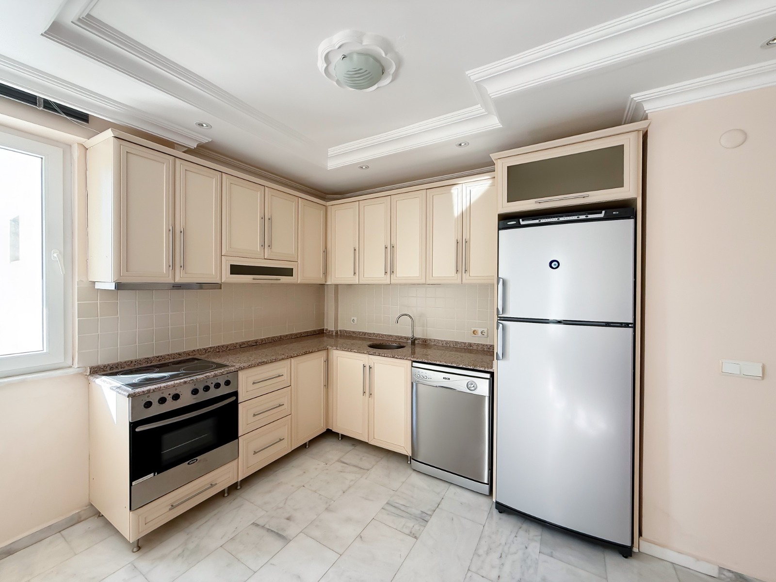 Cream-cabinet kitchen with a granite worktop and silver appliances in an apartment