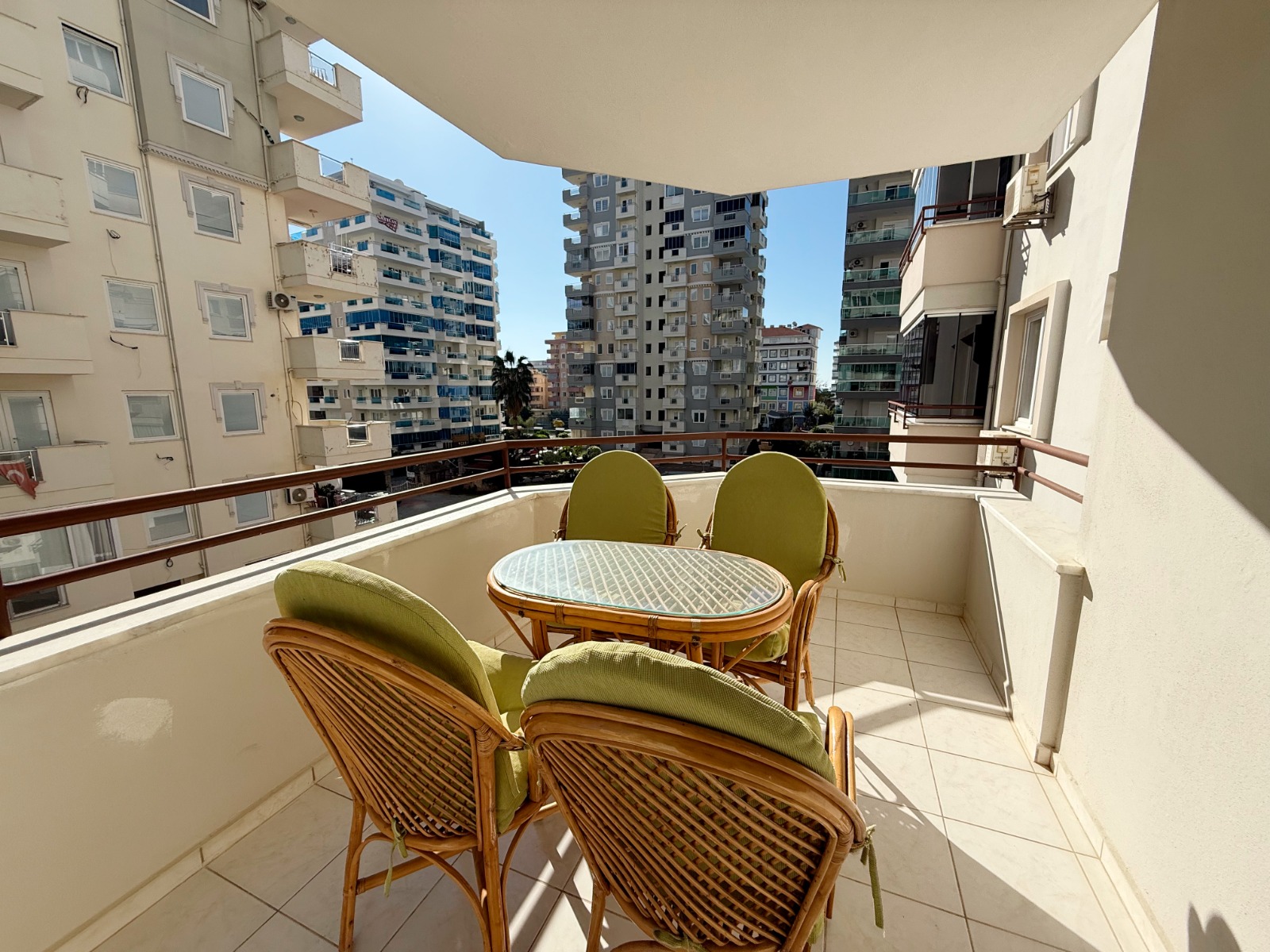 Terrace with a glass table and green cushions beside high-rise buildings in Turkey