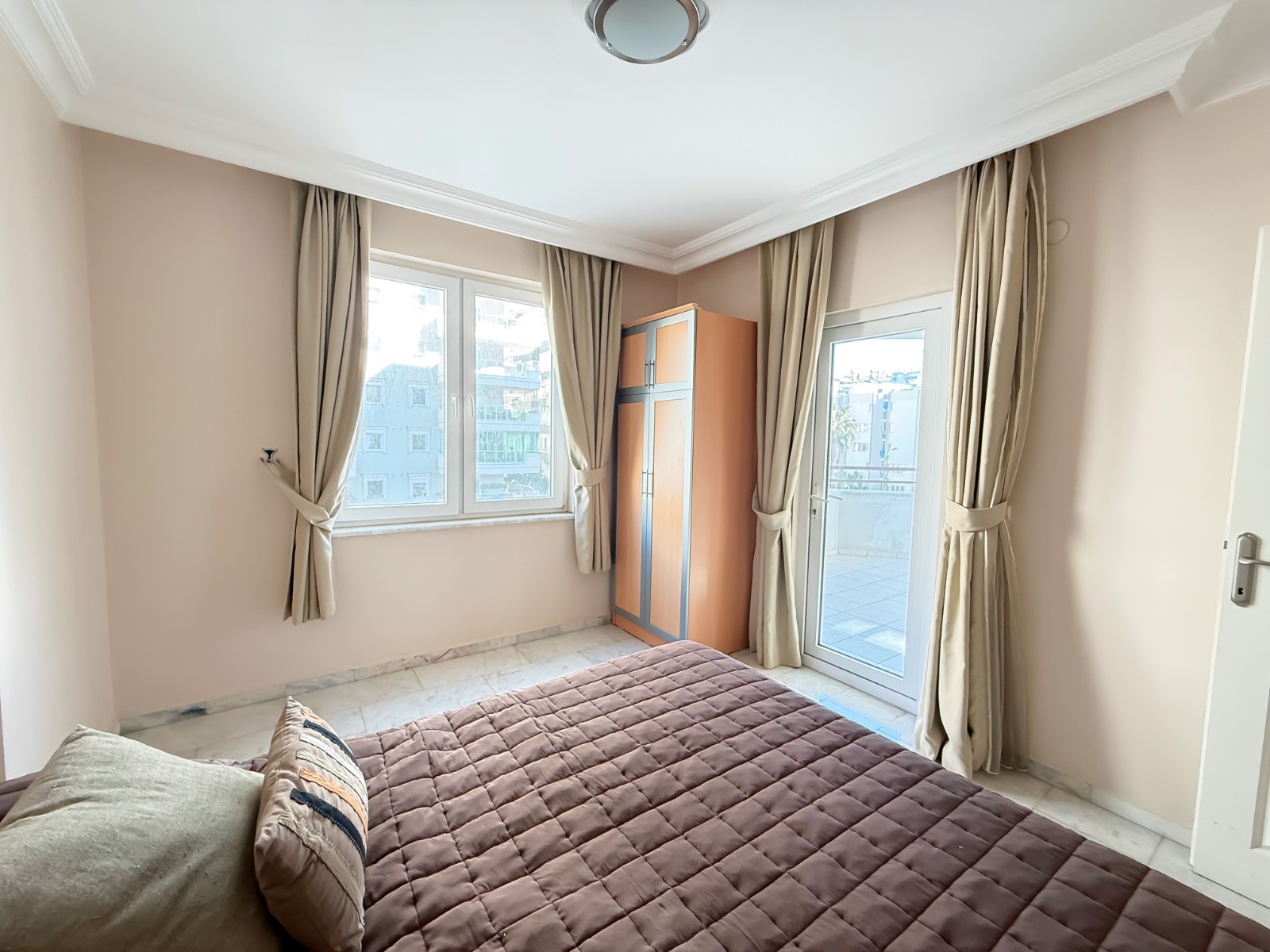 The bedroom has a balcony door and a view of city buildings in Mahmutlar