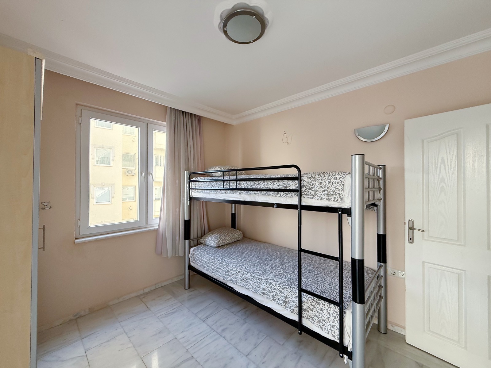 Child's bedroom with a metal bunk bed and curtained window in an apartment