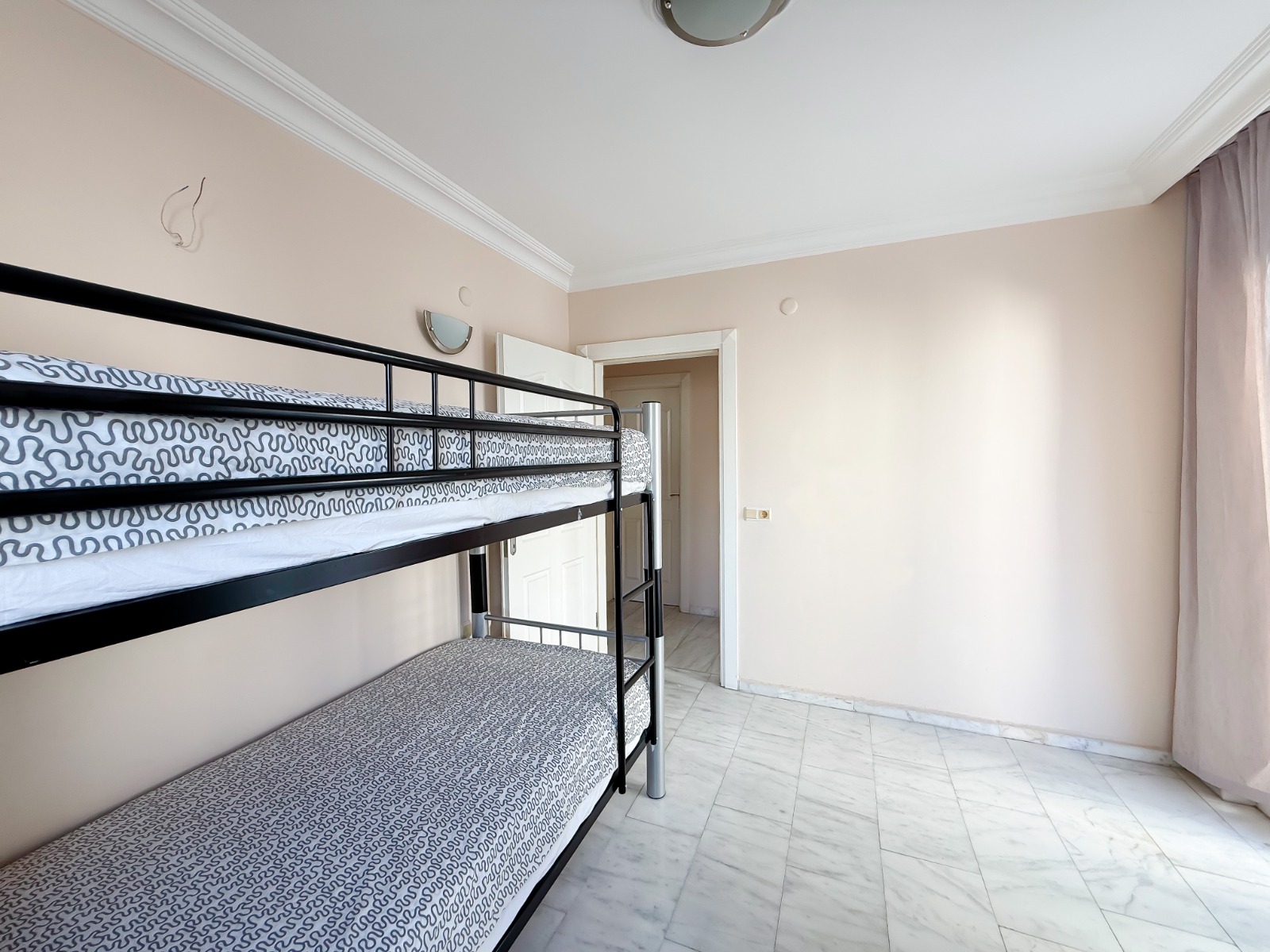 A child's bedroom with a metal bunk bed and window in a flat in Mahmutlar