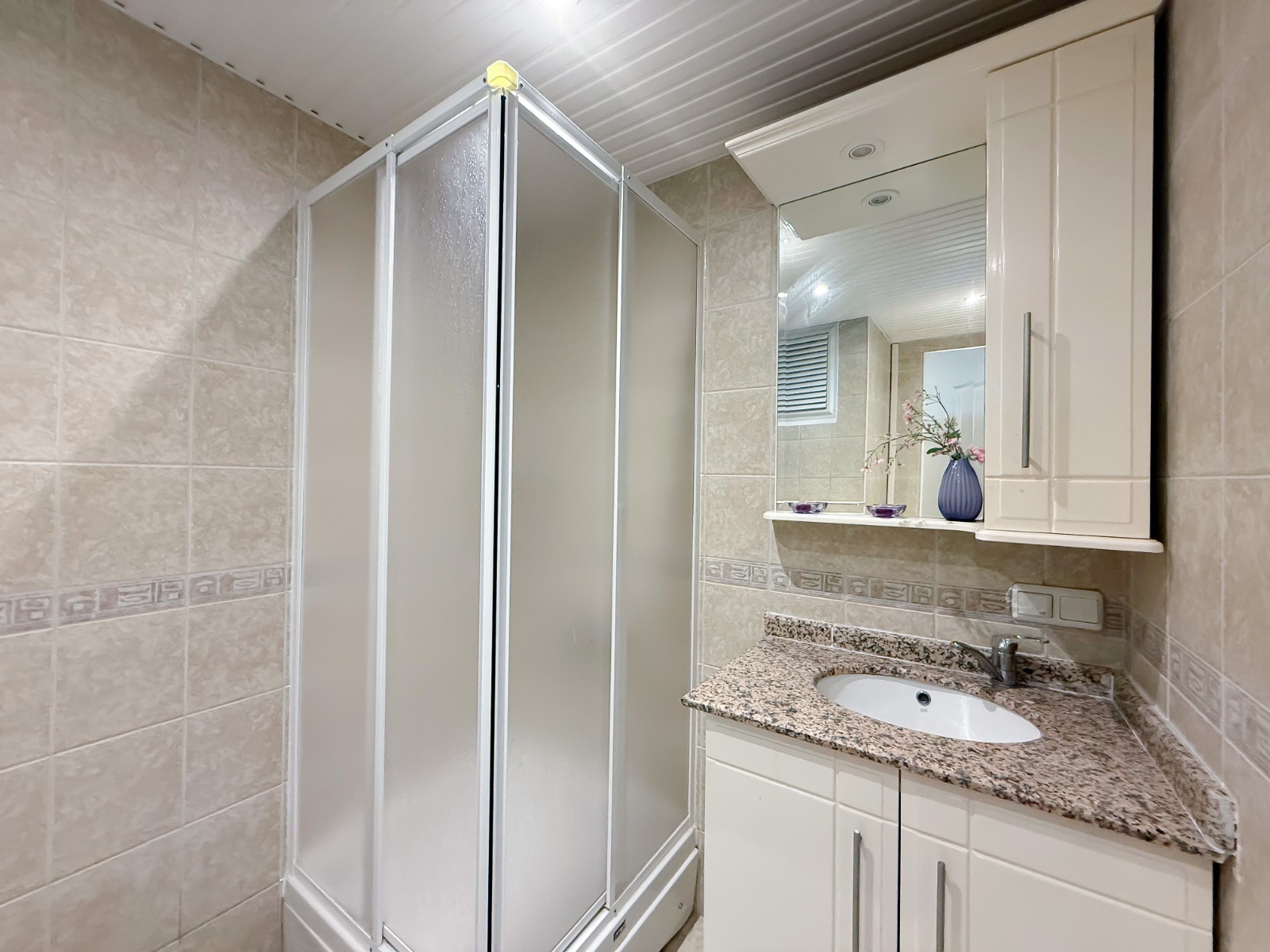 A bathroom with a shower enclosure, mirror and marble vanity in a residence in Mahmutlar
