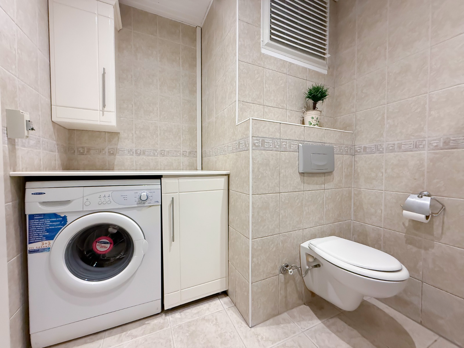 Laundry room with a wall-mounted toilet and washer beneath the counter in a flat