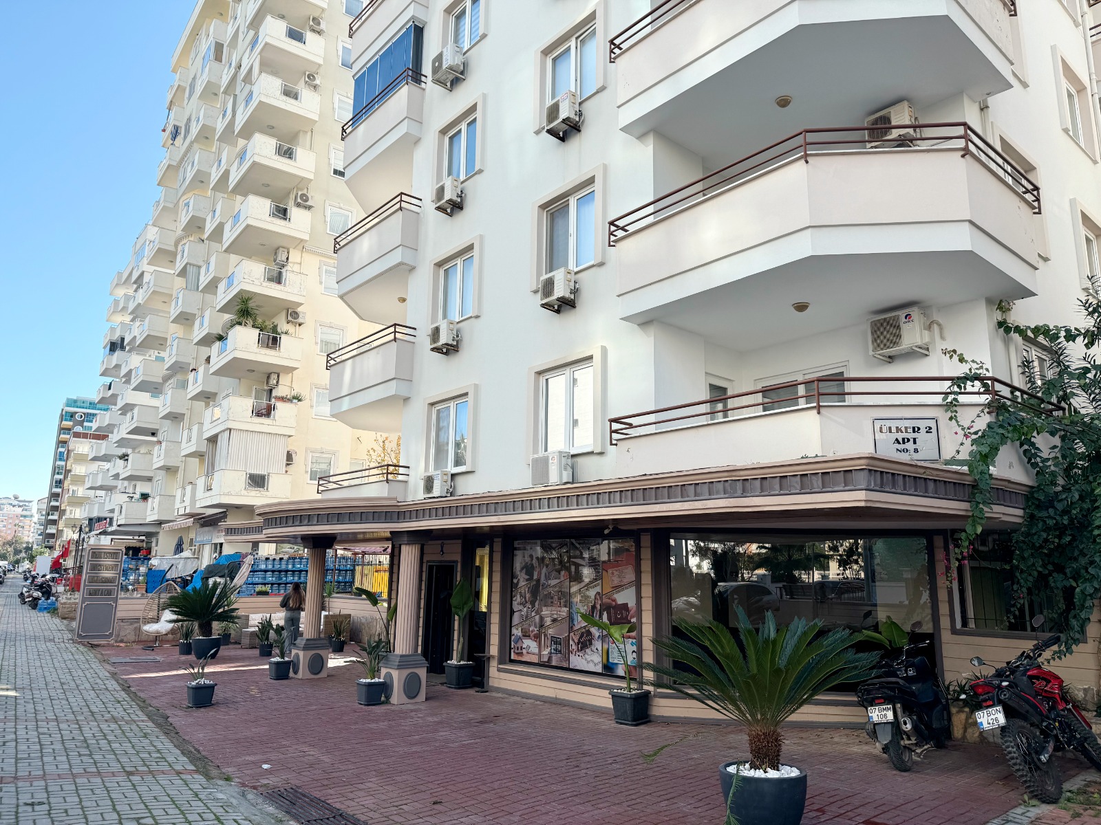 White apartment facade with balconies, air conditioners and motorcycles outside in Mahmutlar, Turkey