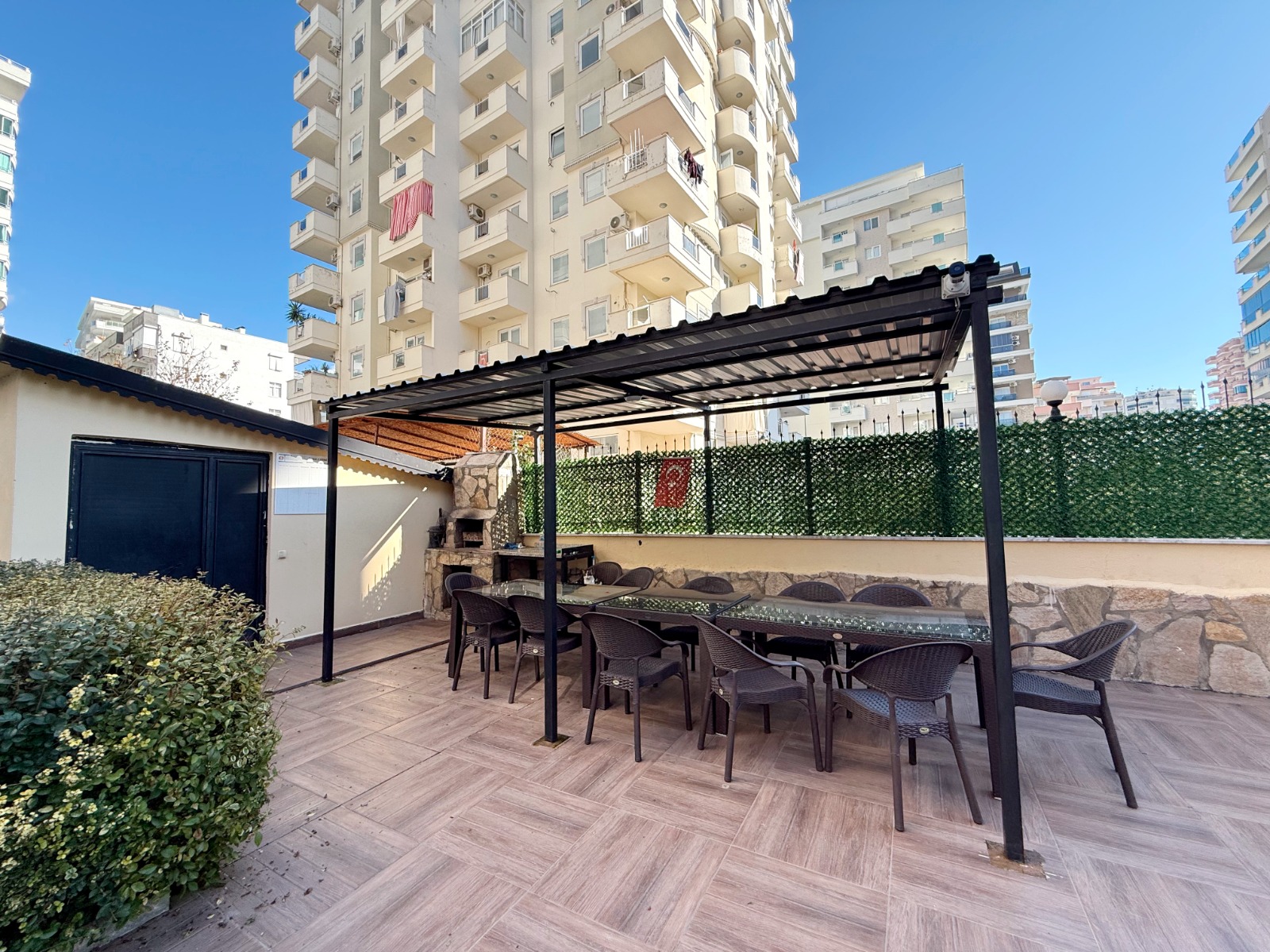Covered dining area with a glass table and garden chairs in a complex with apartments in Turkey