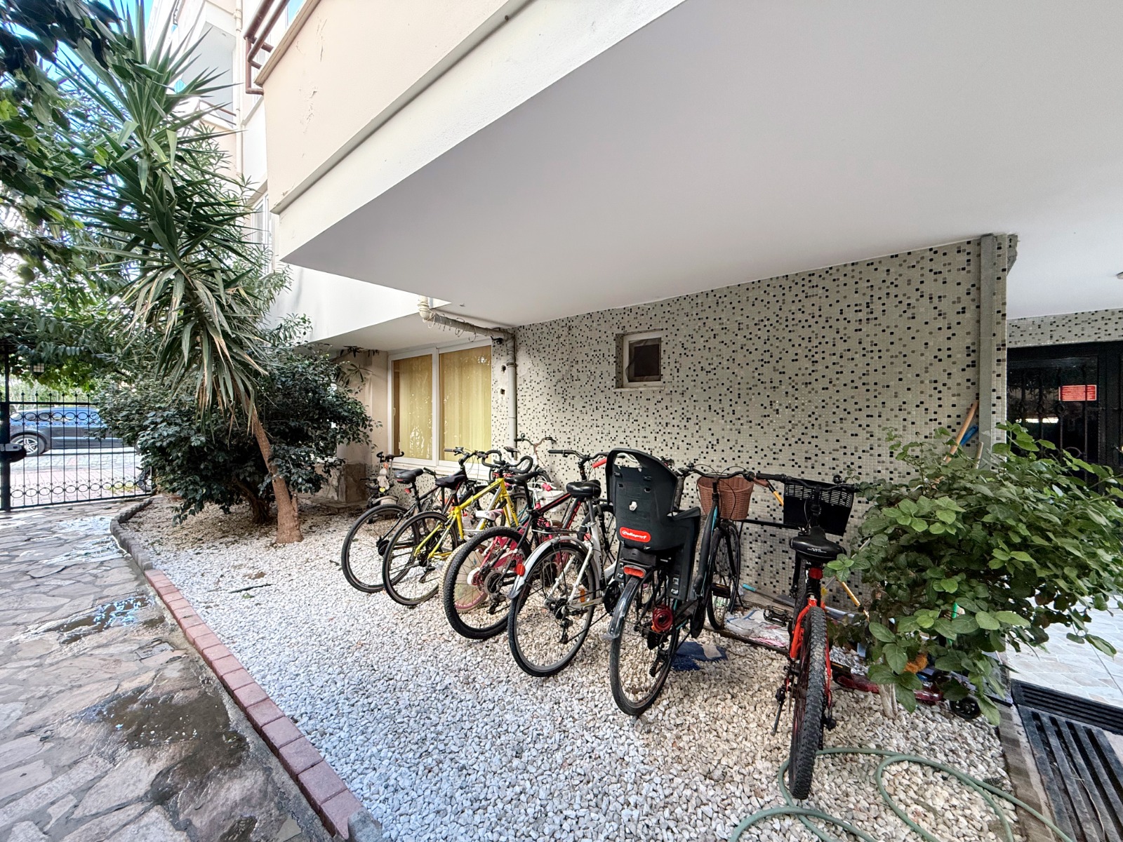 Bicycles under a covered shelter beside a garden path in a complex with apartments for sale in Turkey