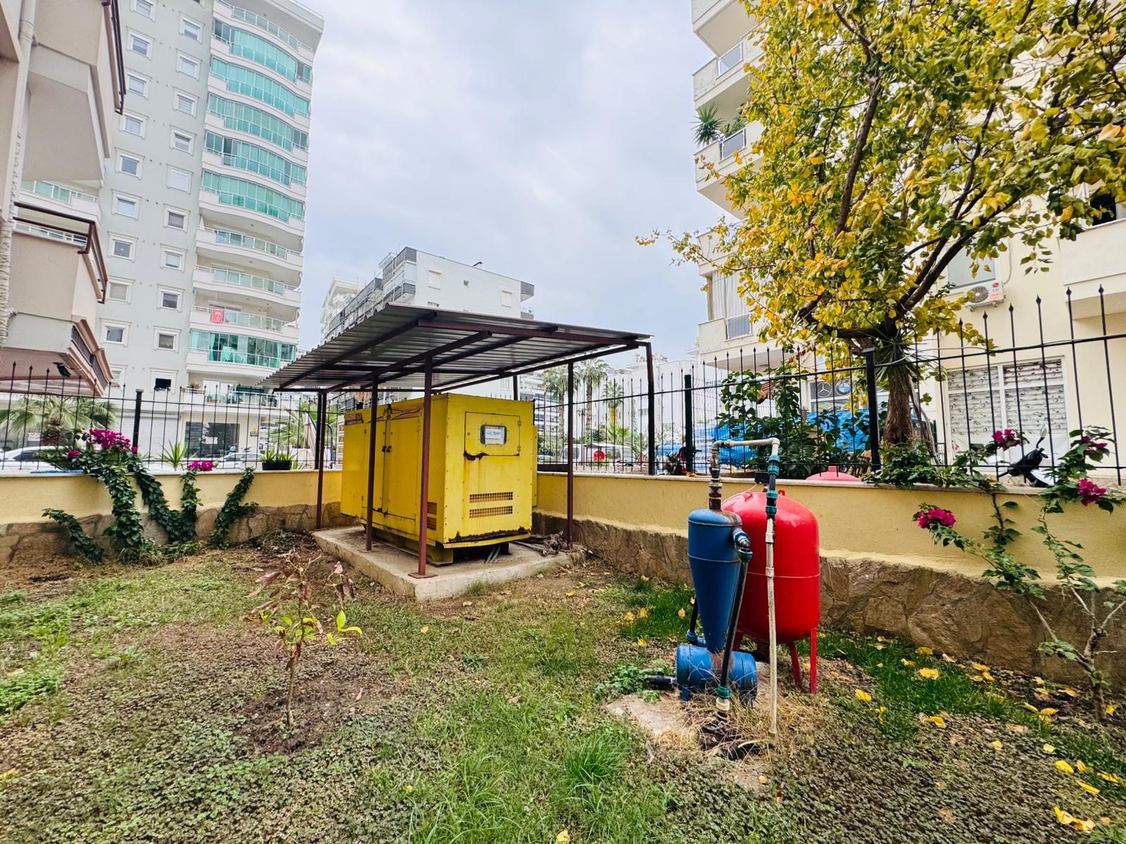 Yellow electrical generator beneath a technical shelter among lawn and flowering shrubs