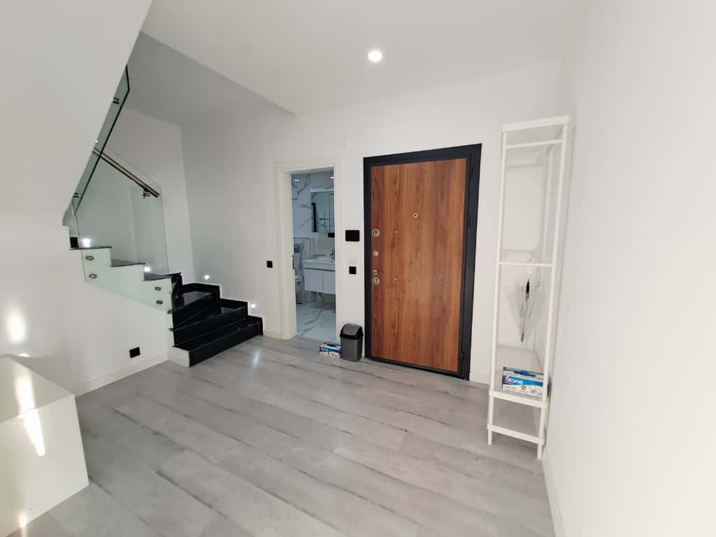 Holde ahşap giriş kapısı ve siyah basamaklı cam korkuluklu merdiven penthouse içinde