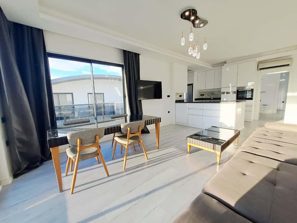 Mutfaklı oturma odasında bej köşe koltuk ve balkona açılan panoramik pencere satışta