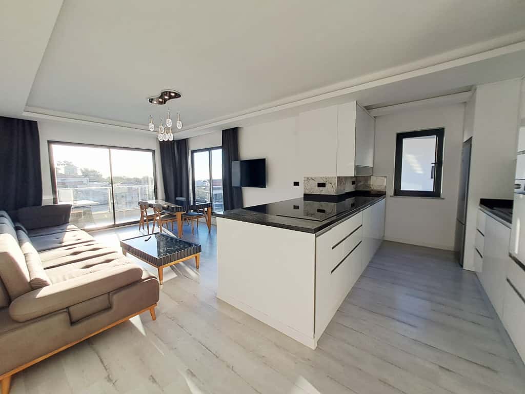 Mutfaklı oturma odasında beyaz ada ve siyah tezgâh penthouse dairenin içini gösteriyor