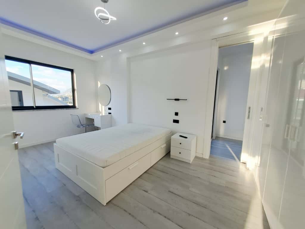 Yatak odasında beyaz yatak ve yuvarlak aynalı makyaj masası penthouse dairede bulunuyor