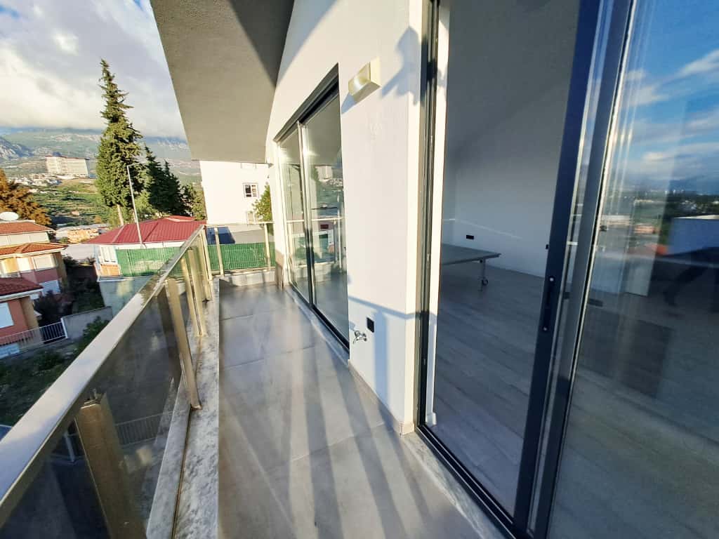 Balkon boyunca sürgülü camlar ve kırmızı çatılı komşu evler penthouse dairenin yanında