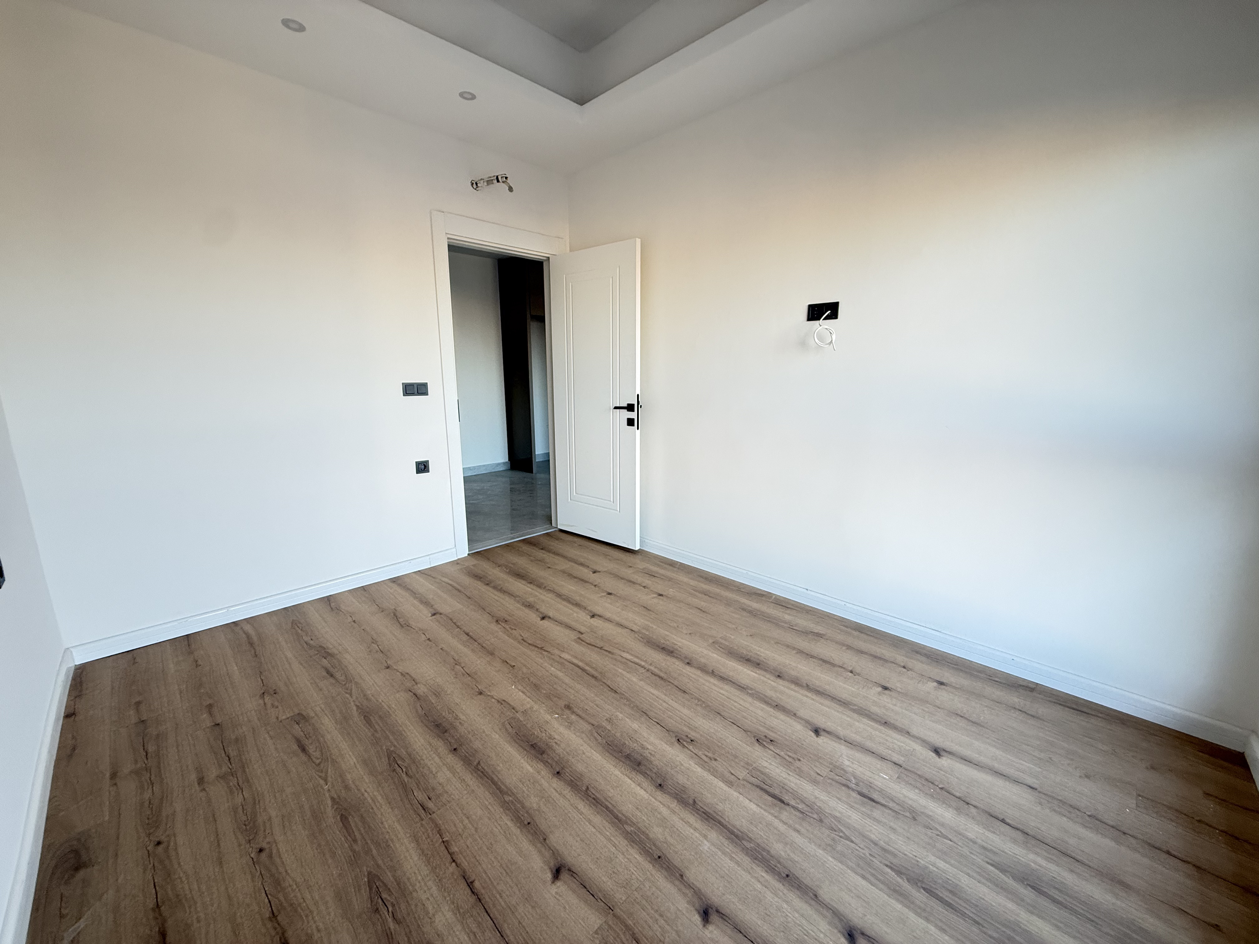 Bright room with wood-effect laminate and a white door opening to the corridor in Turkey