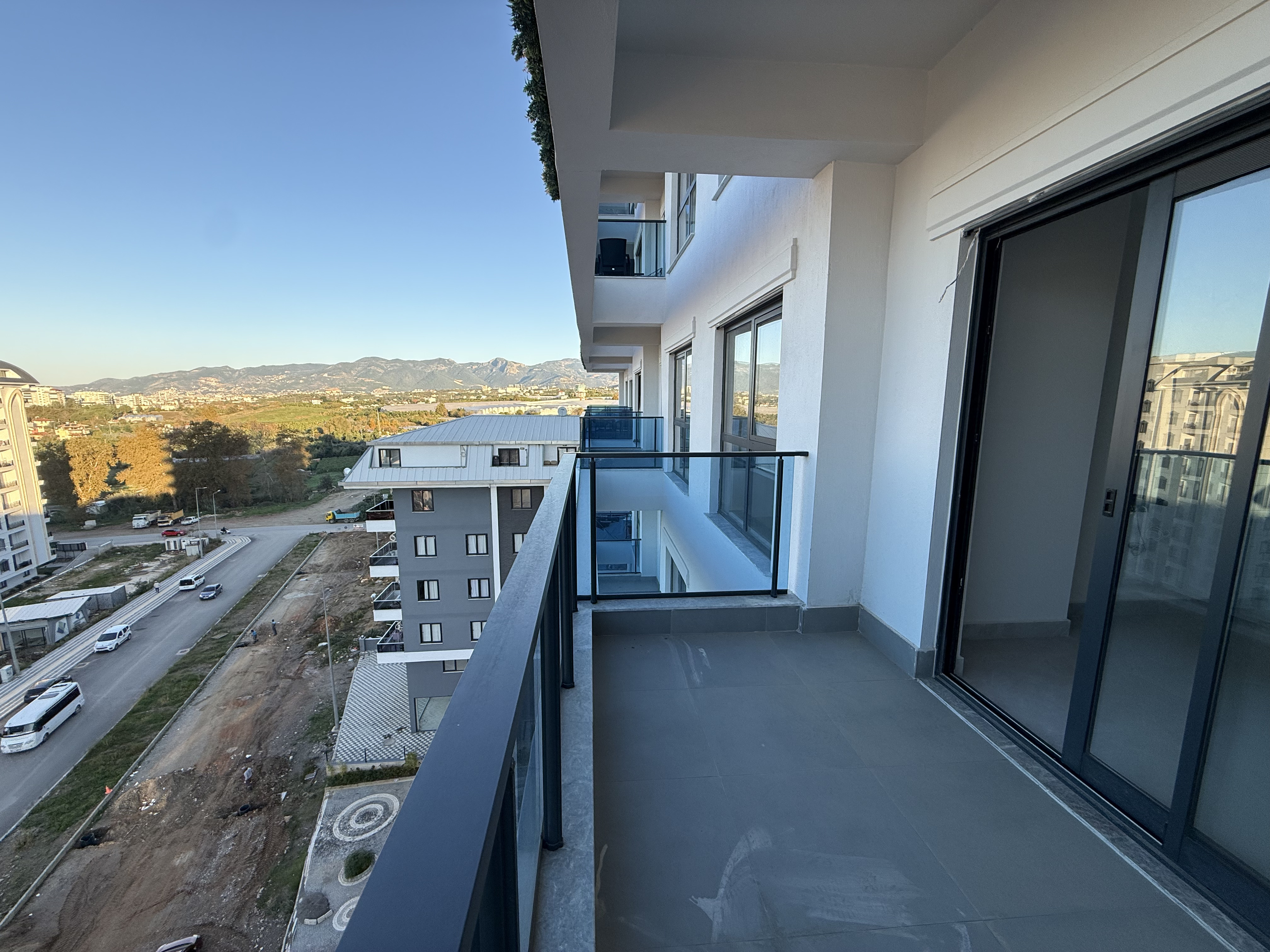 Long balcony with sliding doors and glass railing facing a mountain ridge near Mahmutlar in Turkey