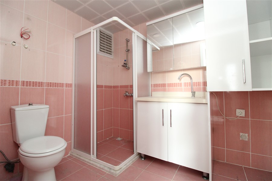 Pembe seramikli banyo cam duş kabini ve beyaz lavaboyla düzenlenmiş