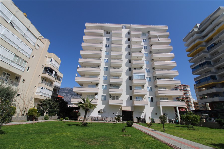 White multi-storey residential building with balconies and a palm in a flat complex in Mahmutlar, Turkey
