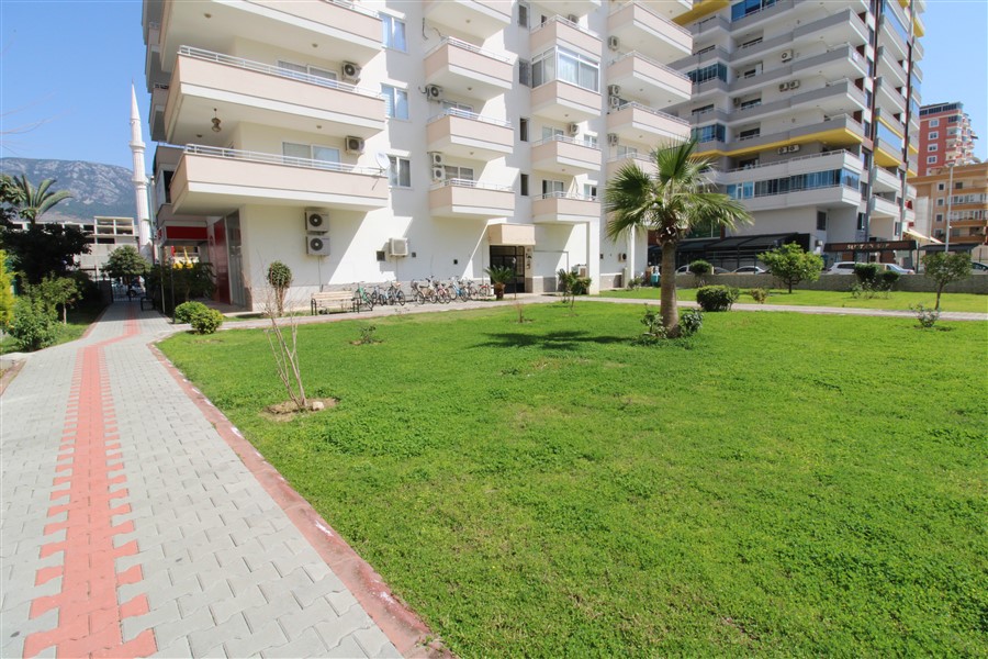 Green lawn and tiled walkway beside a residential building in Turkey where apartments are for sale