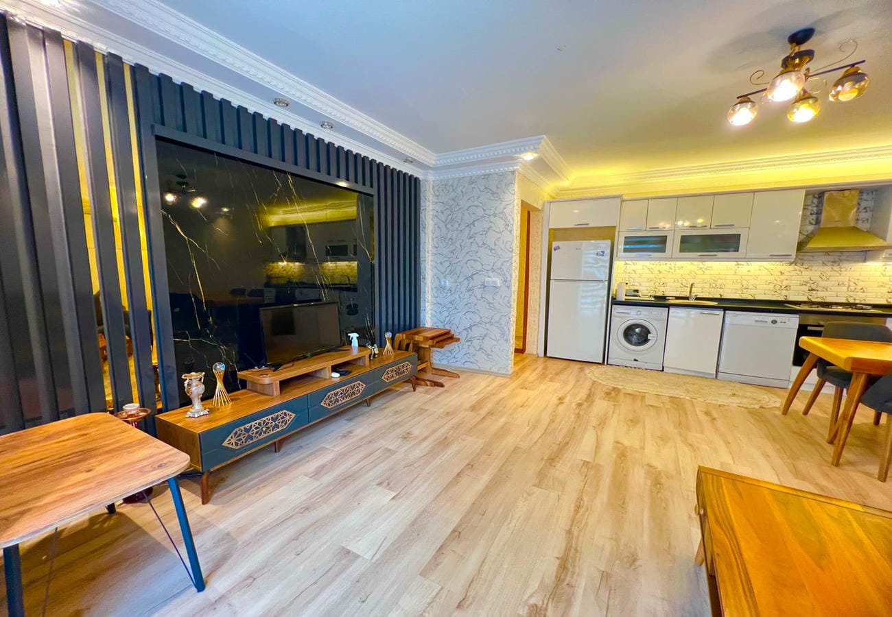 Televizyonlu mutfak-salon, beyaz dolaplar ve açık ahşap zeminiyle Mahmutlar’daki dairede