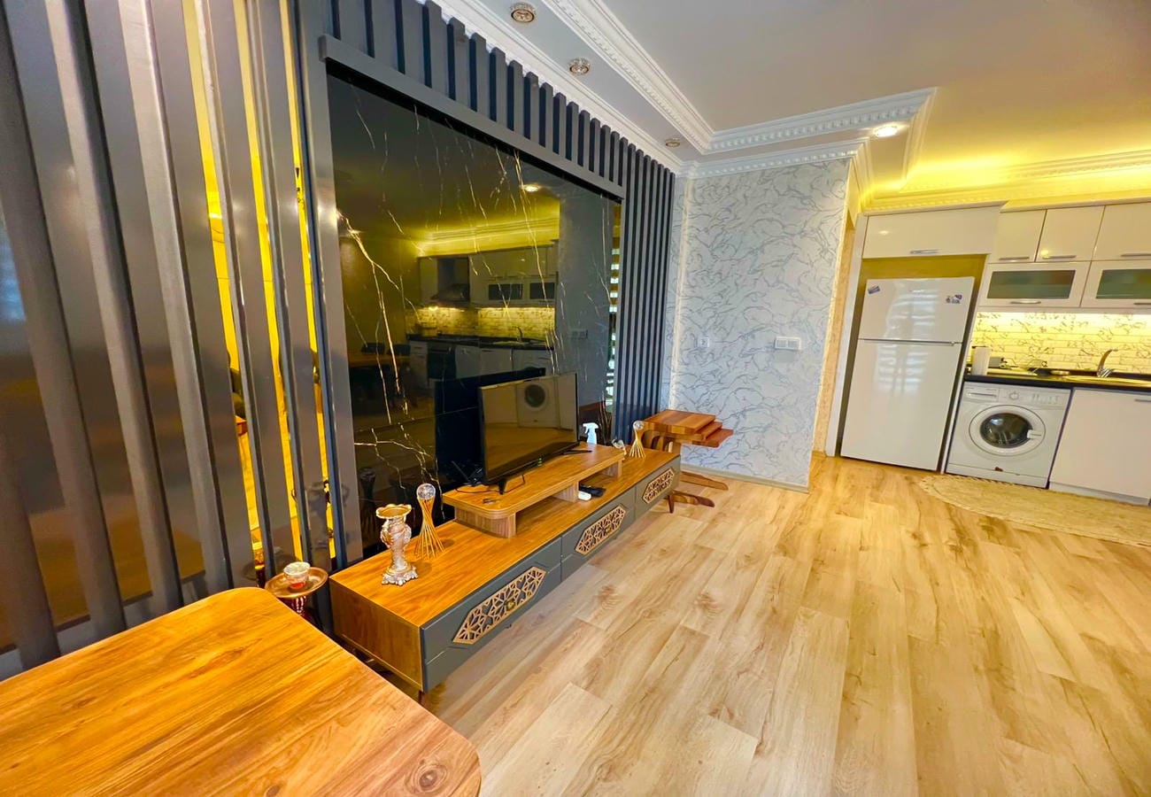Televizyonlu salon, ahşap konsol ve beyaz mutfakla Mahmutlar’da satışta olan yaşam alanında