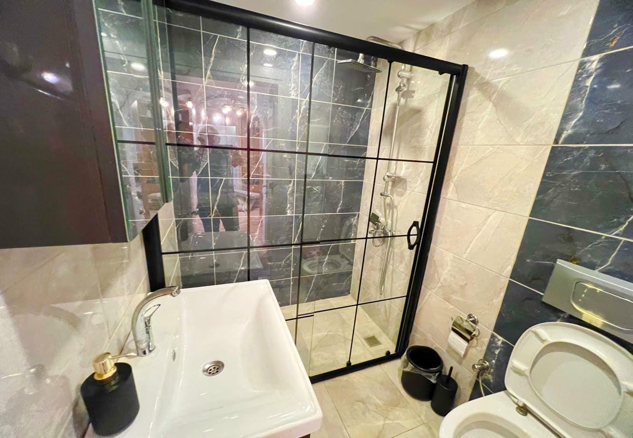 Beyaz lavabo, siyah çerçeveli duş bölmesi ve klozet bulunan banyo