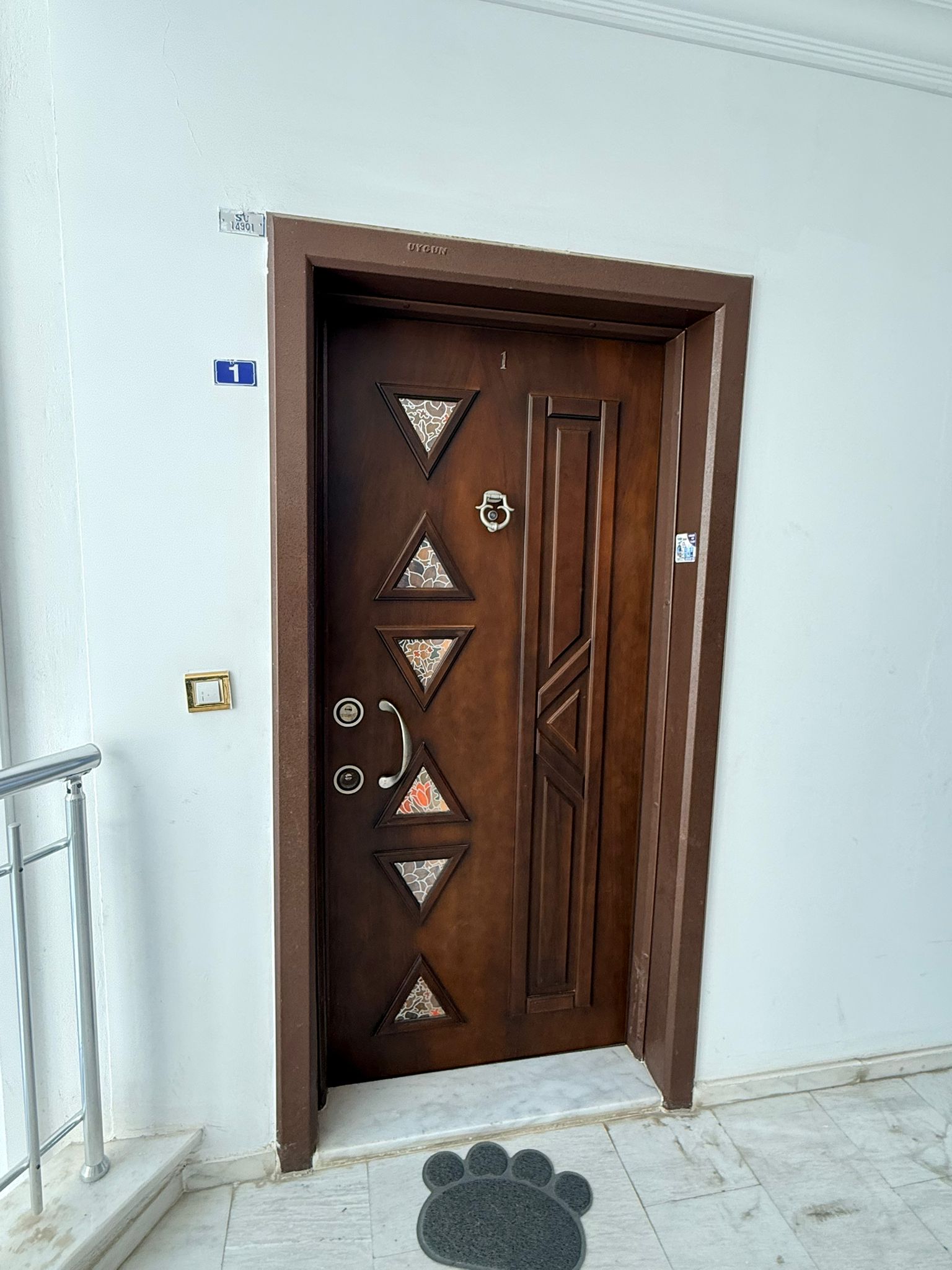 Koyu ahşap detaylı kapalı daire kapısı, mermer zeminli koridorun metal korkulukları yanında