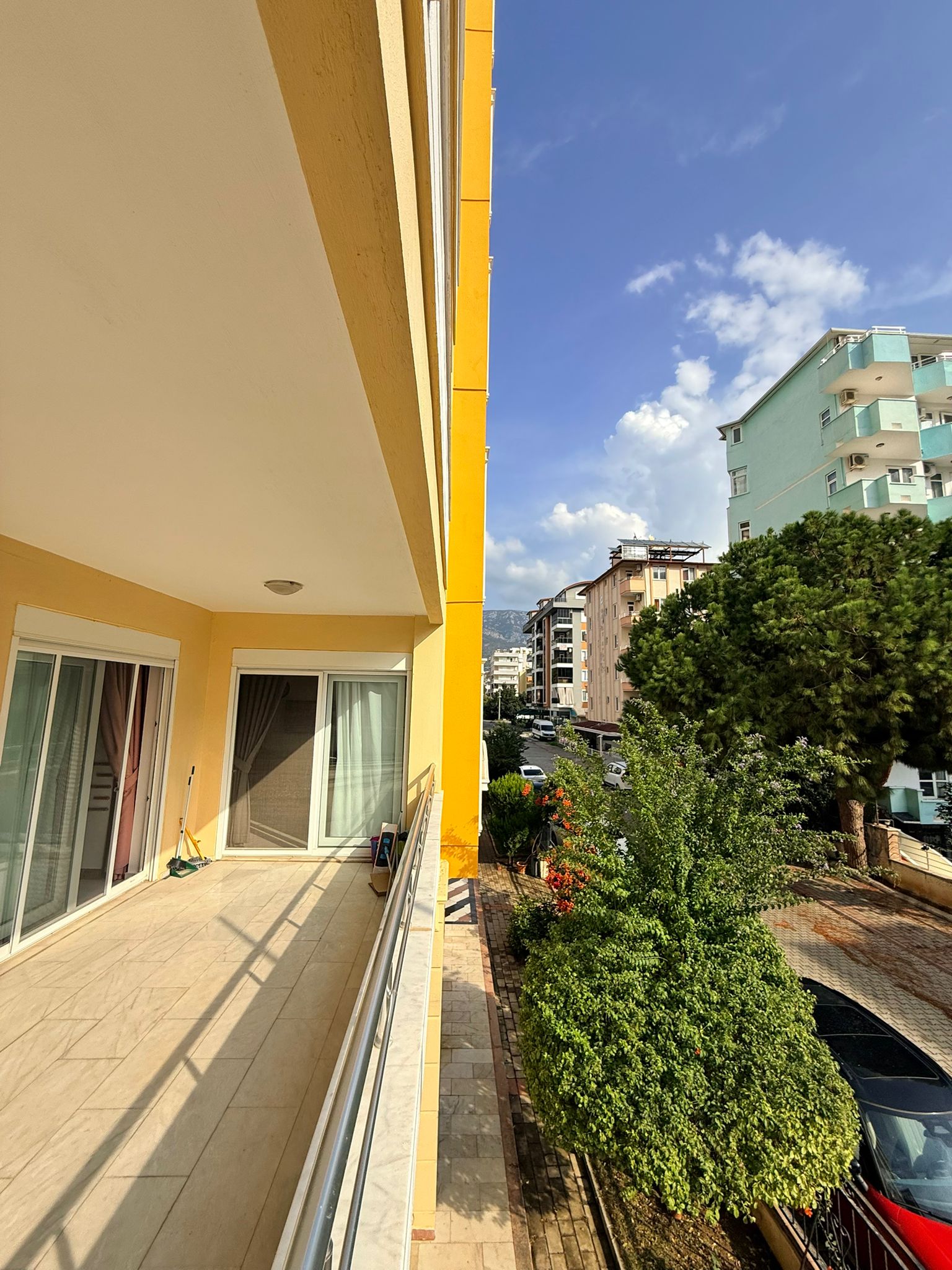 Uzun kapalı teras, Türkiye'de dairelerin bulunduğu sitede sürgülü cam kapılar ve yeşil ağaçlarla
