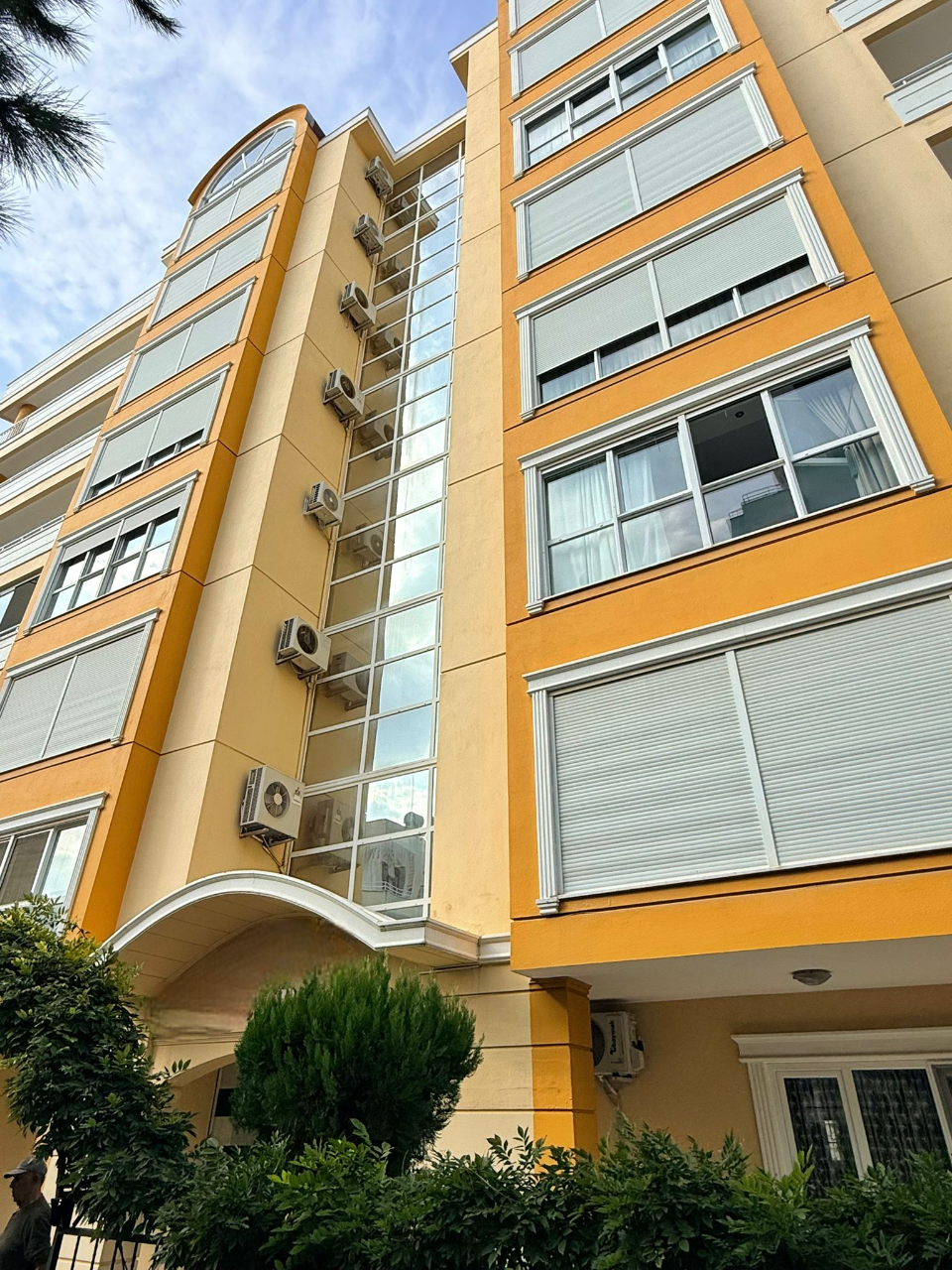 Mahmutlar'daki konutun sarı-bej cephesinde panoramik merdiven camları ve klima üniteleri