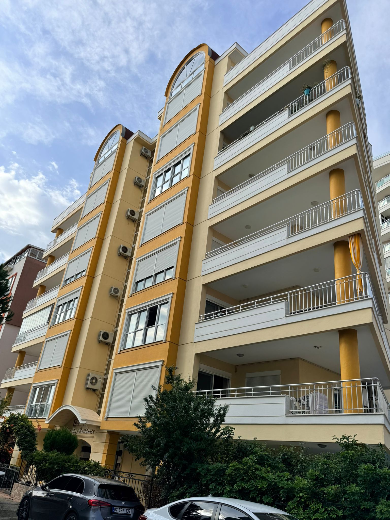 Mahmutlar'da satışta olan dairenin bulunduğu binada geniş balkonlar ve sarı yuvarlak kolonlar