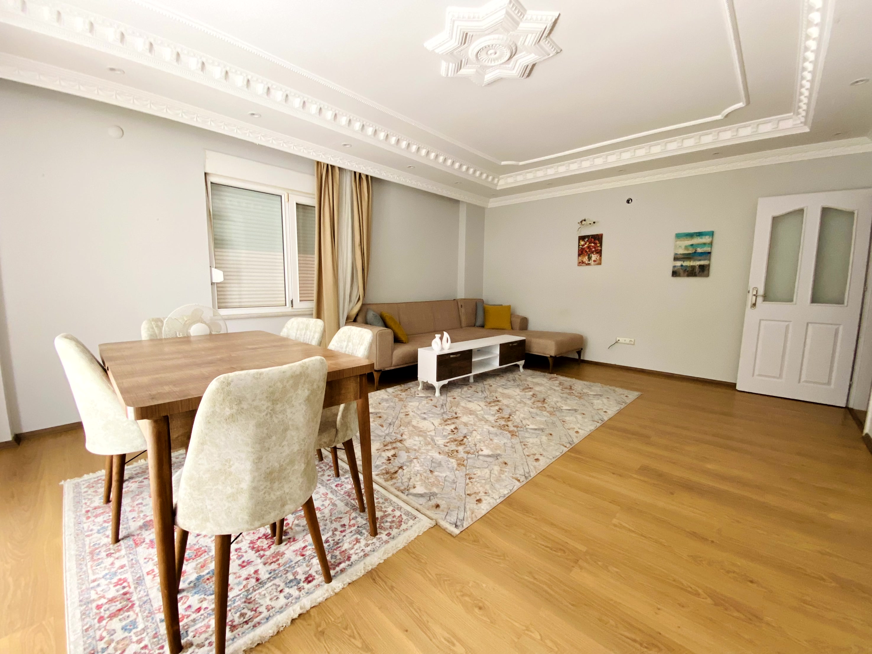 Bej köşe koltuklu salon ve yemek masası bulunan dairede panoramik pencere