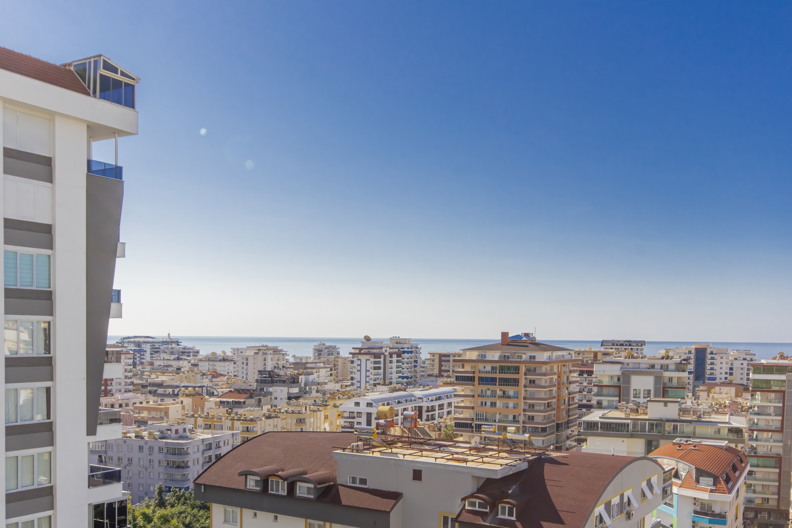 Satıştaki konuttan şehir ve deniz panoraması, kırmızı çatılı binalar ve açık mavi gökyüzü