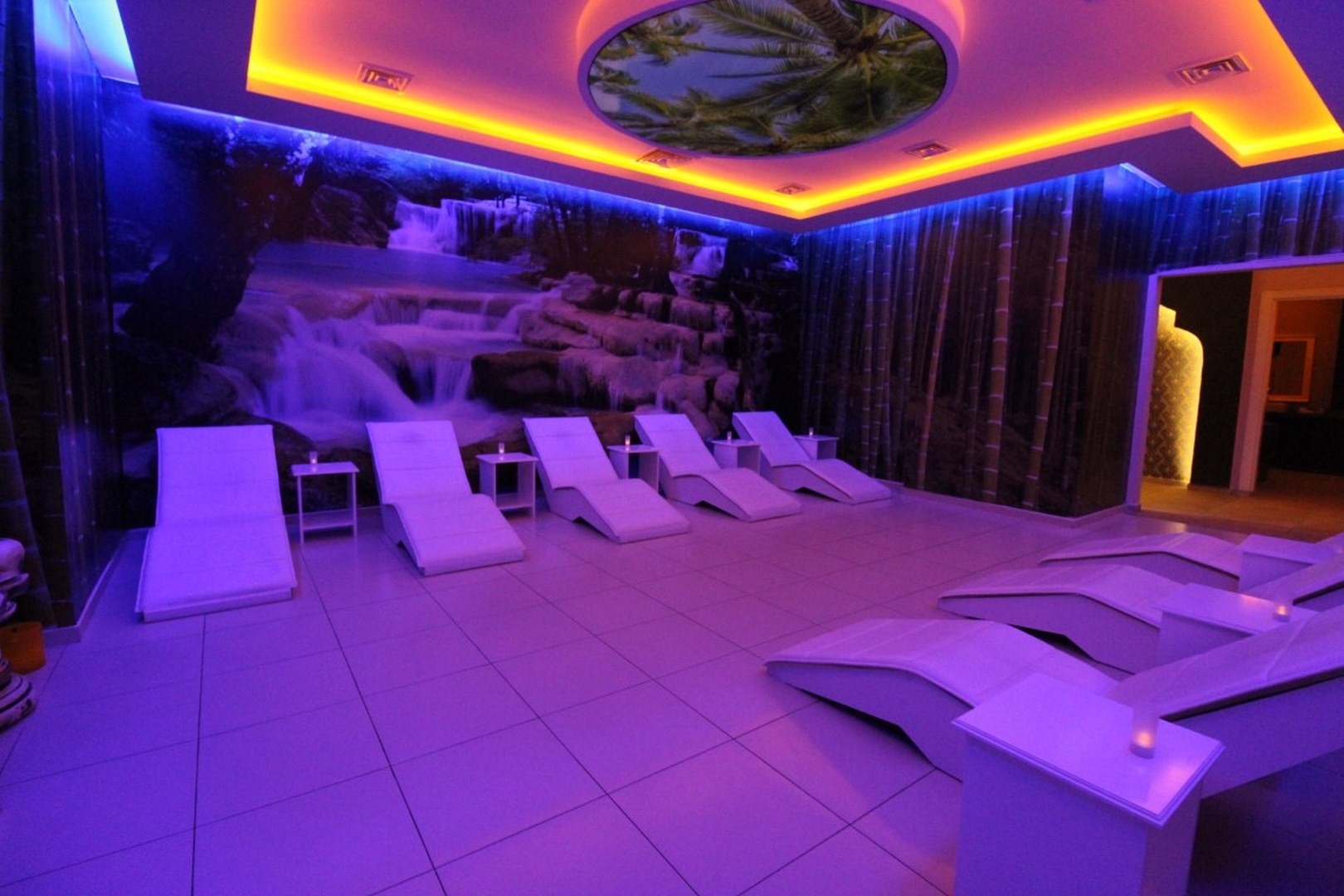 Mahmutlar’daki spa alanında beyaz şezlonglar, şelale panosu ve mor-mavi aydınlatma