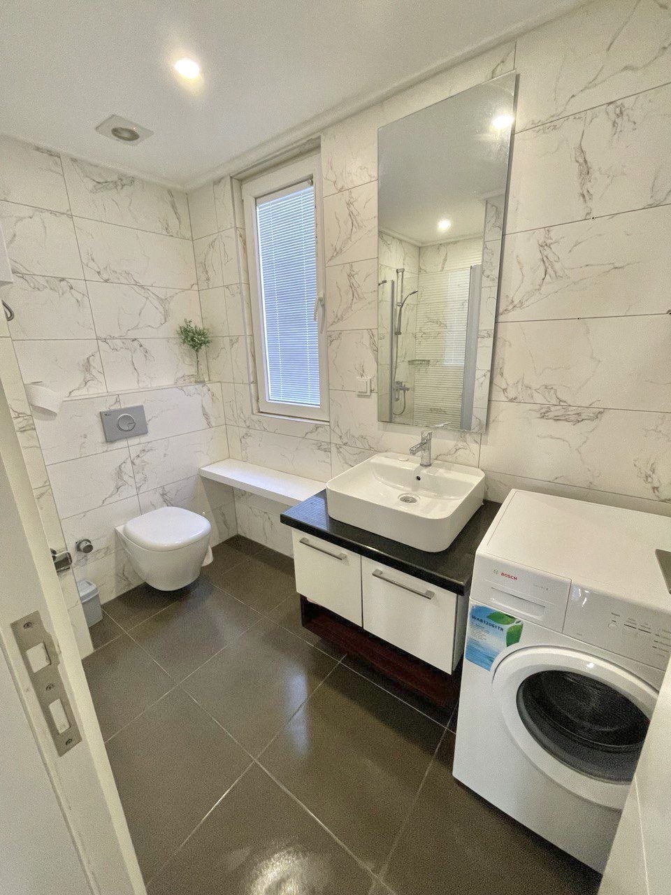Mermer duvarlı banyo, Mahmutlar’daki dairede siyah tezgâhlı lavabo ve çamaşır makinesiyle