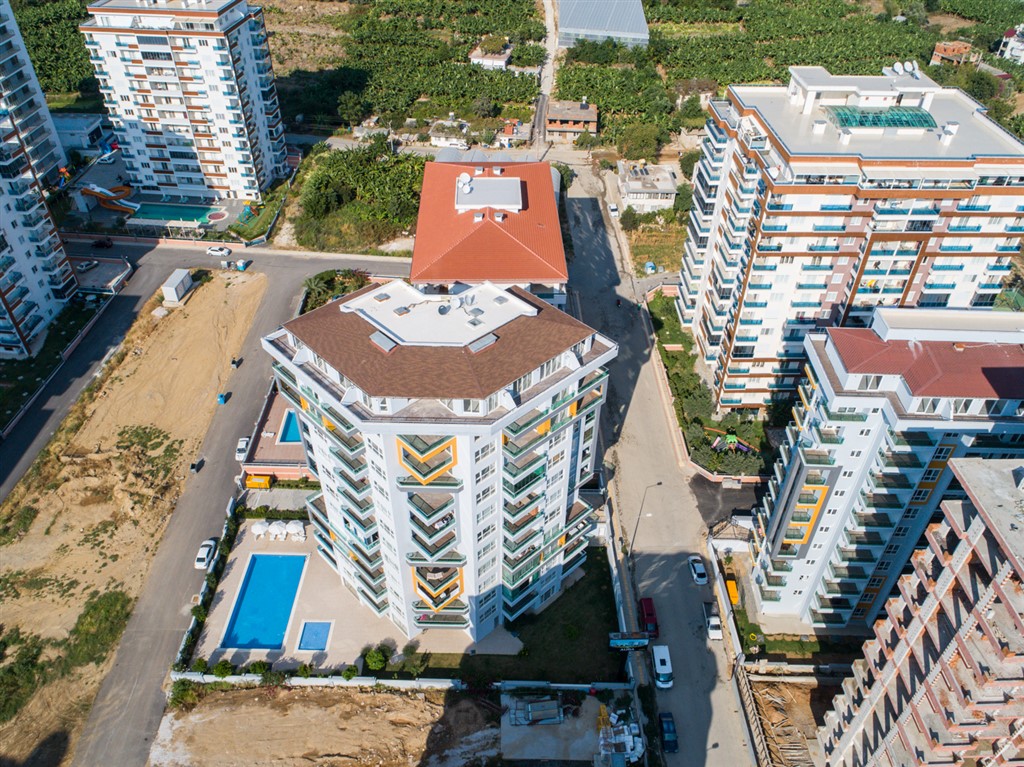 Kırmızı eğimli çatılı kompleks ve açık havuz satışta, şehir yolları ile tarım alanları arasında