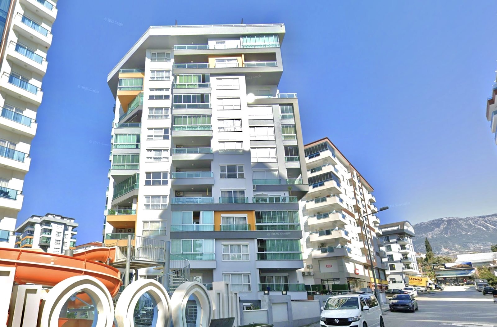 Turuncu panelli çok katlı konut cephesi ve kemerli giriş Mahmutlar’da dağ sırtına bakıyor