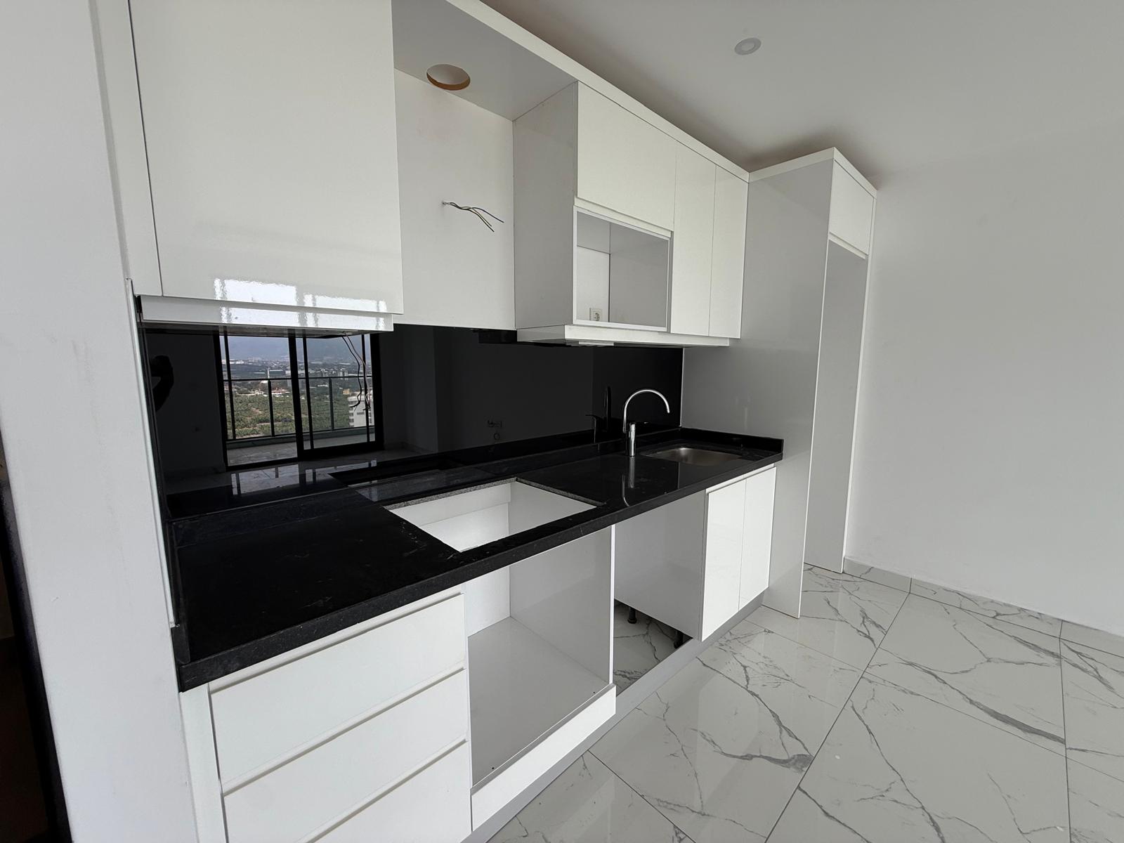 Kitchen with a corner white cabinet run and city view through the window in Mahmutlar