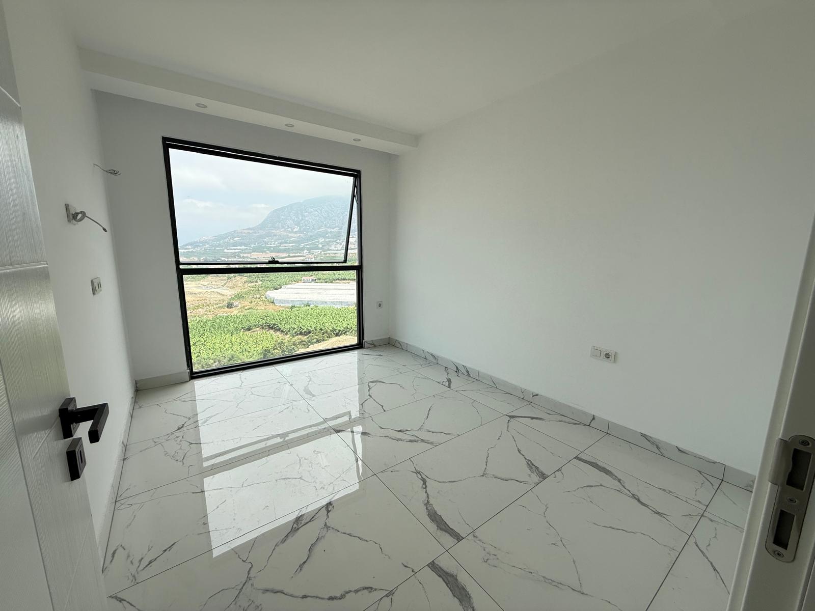 Bedroom with a sloped panoramic window and mountain view in an apartment in Mahmutlar