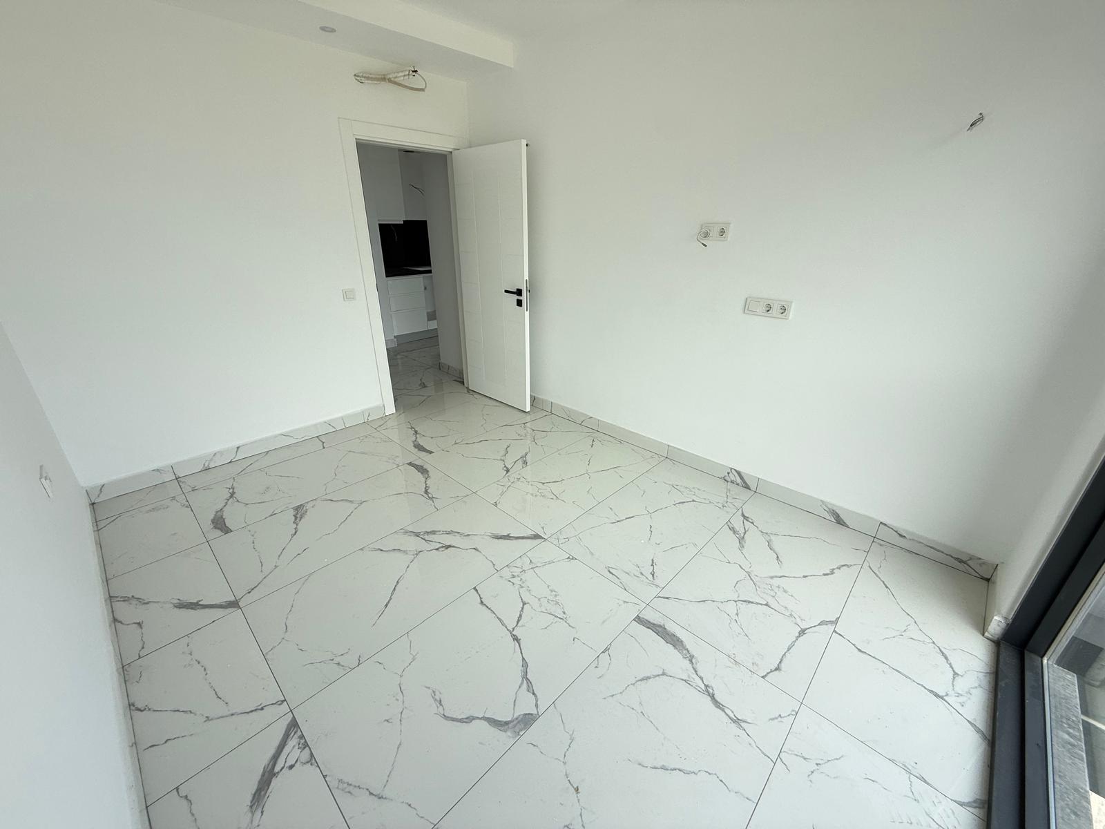 Bedroom with white walls, grey-veined flooring and a doorway to the window area in Mahmutlar