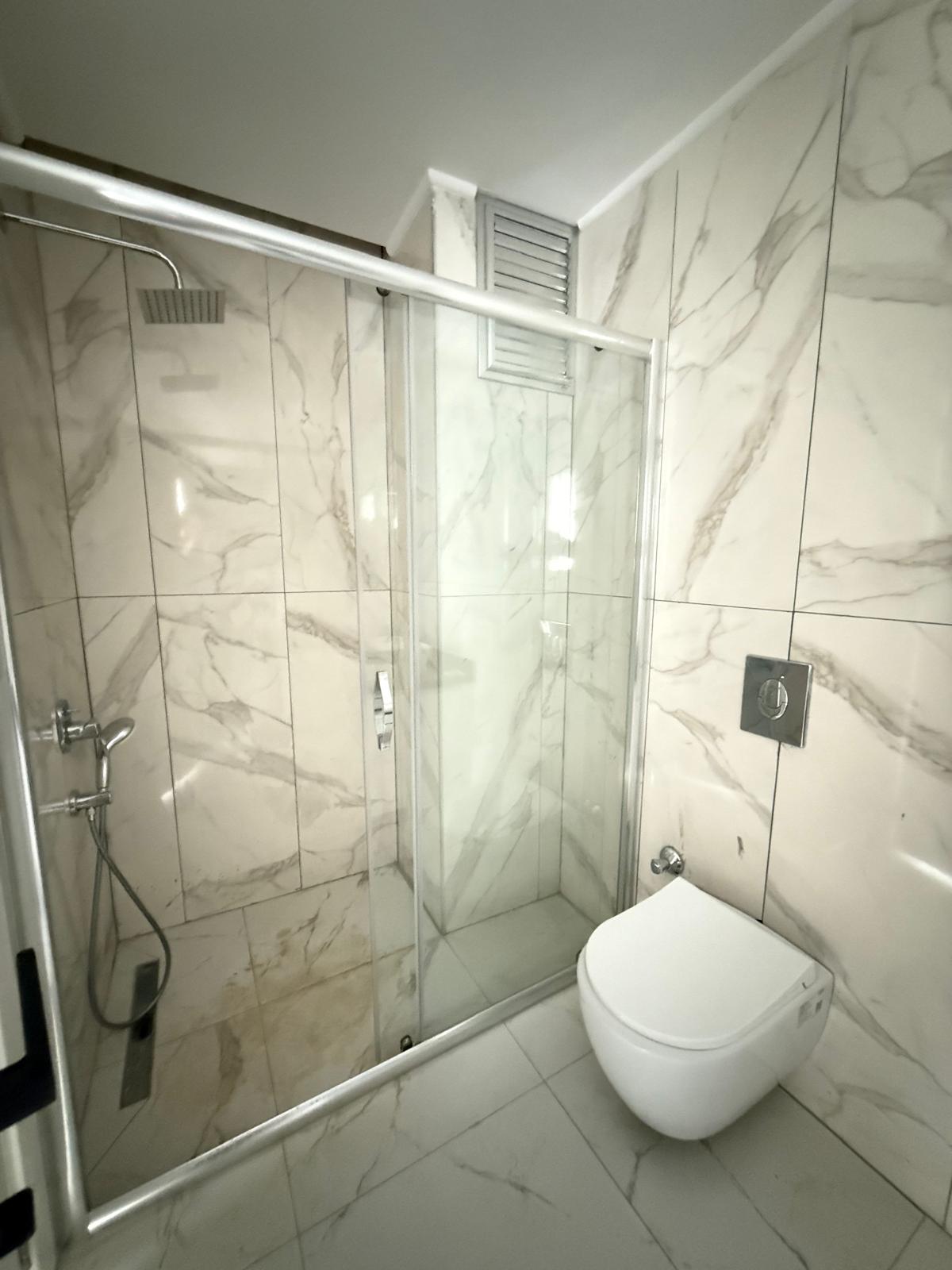 Bathroom with a glass shower enclosure and marble walls and floor in a flat in Mahmutlar