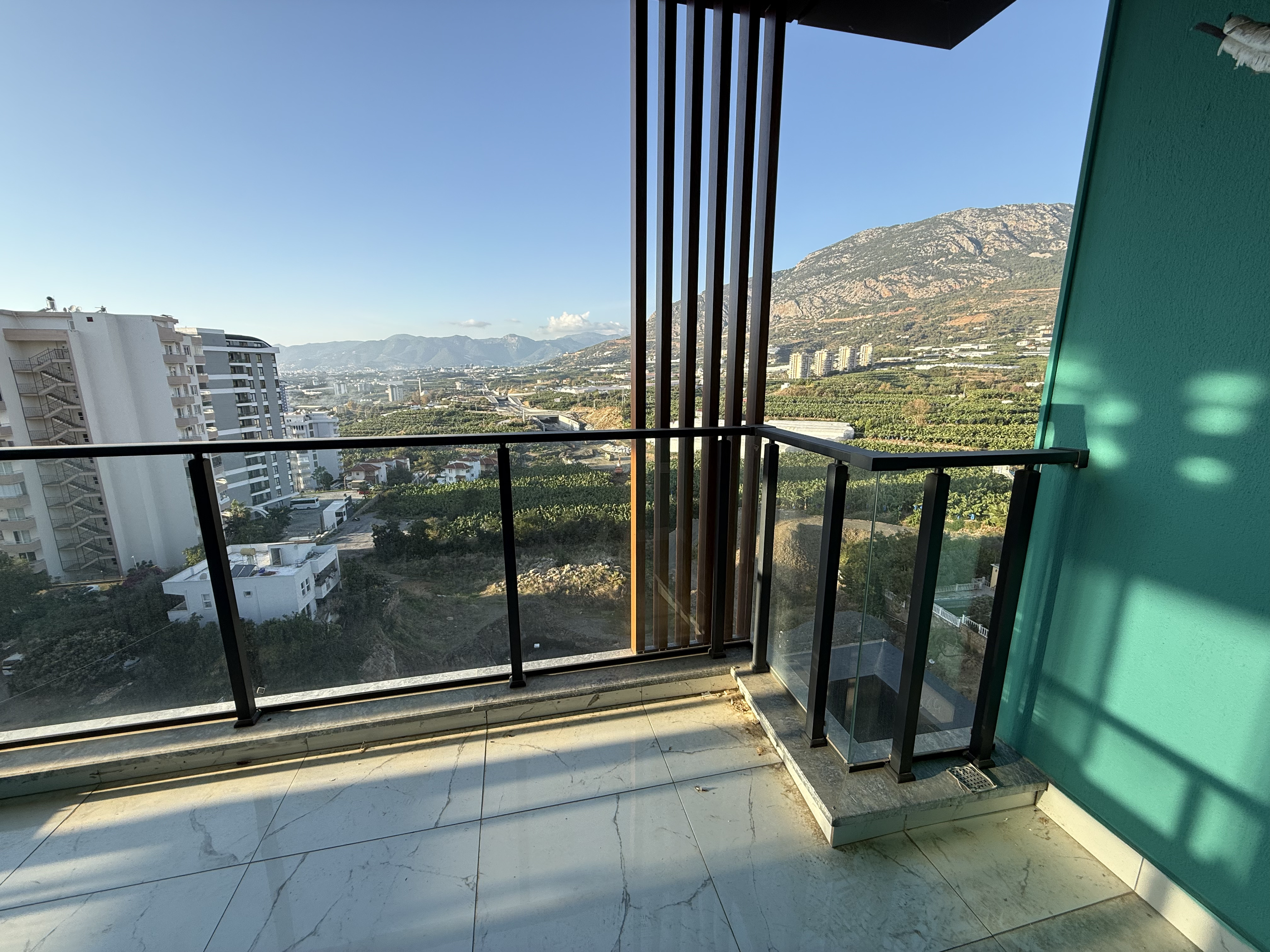 Corner balcony with panoramic glazing and a mountain slope view at a residence in Mahmutlar
