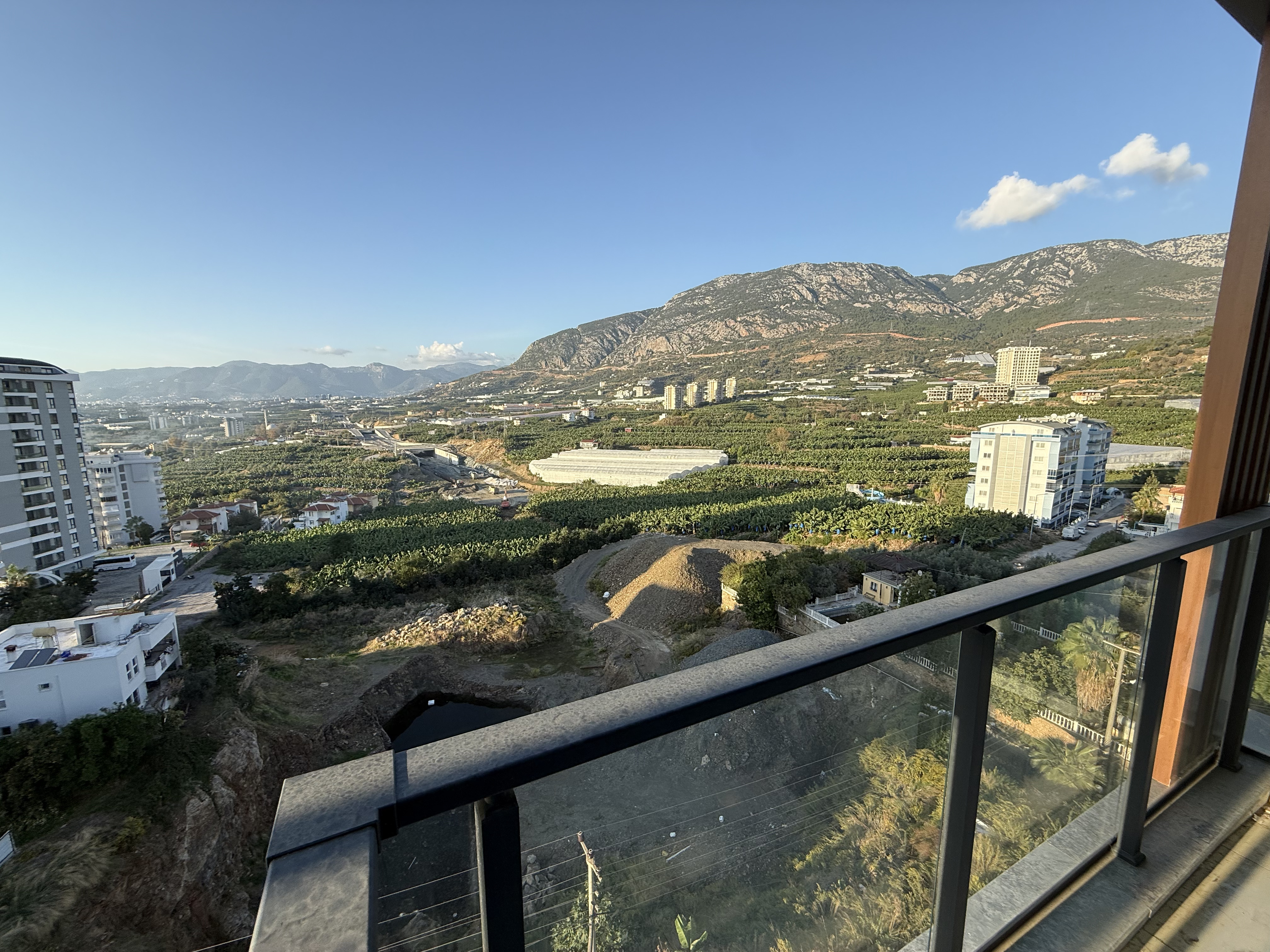 Balcony with glass railing overlooking green plantings and a mountain ridge at a flat