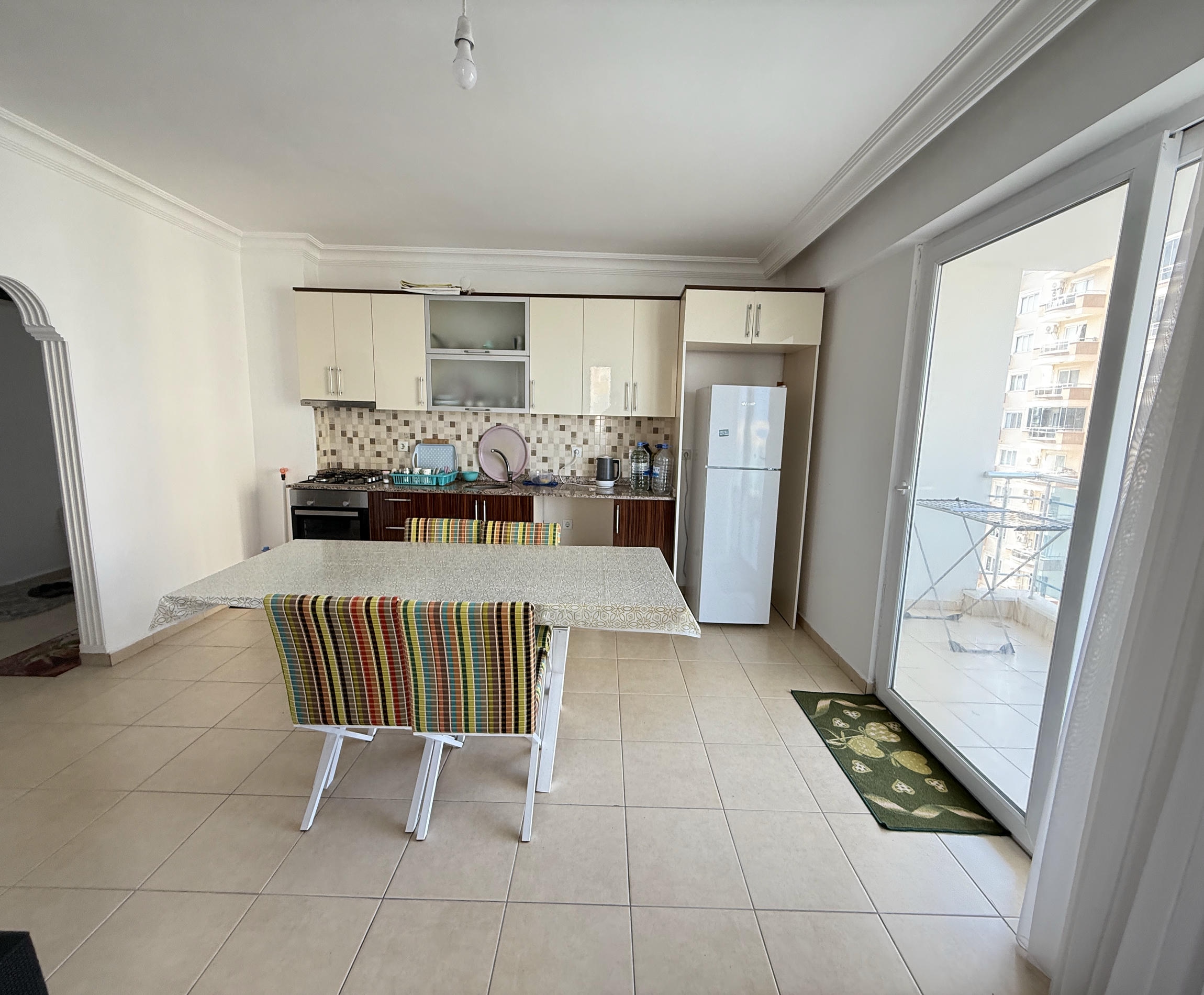 Krem mutfak dolaplı mutfak-salonlu dairede ankastre gazlı ocak ve balkon kapısı bulunuyor